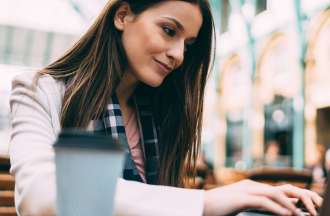[Featured Image] A penetration tester sits outdoors with a cup of coffee and uses her laptop to look for potential cybersecurity financial sector jobs. 
