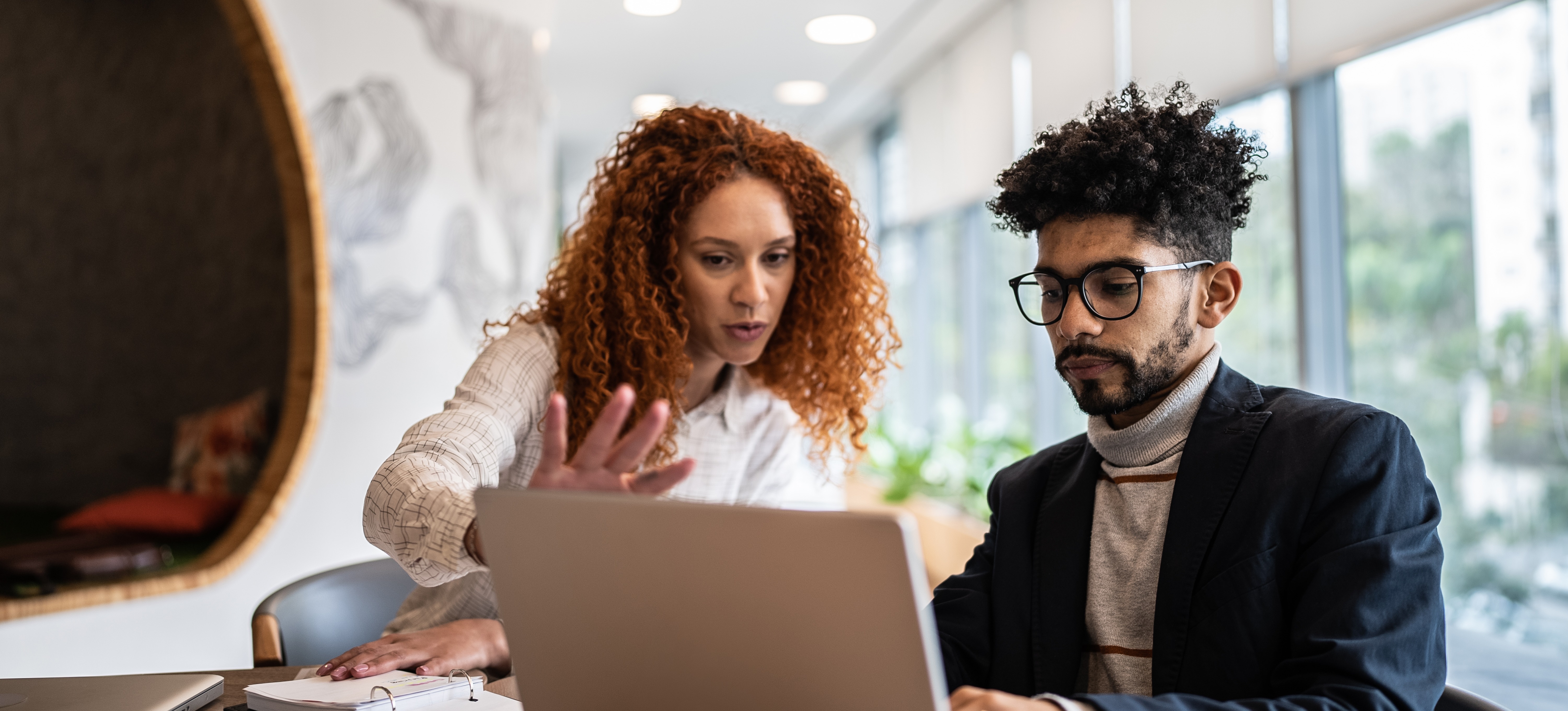 [Featured Image] Two analysts look at a computer screen and discuss data governance certification options online.
