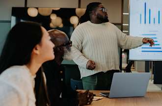 [Featured image] A data analyst presents visualizations from a company data source on a large digital screen.