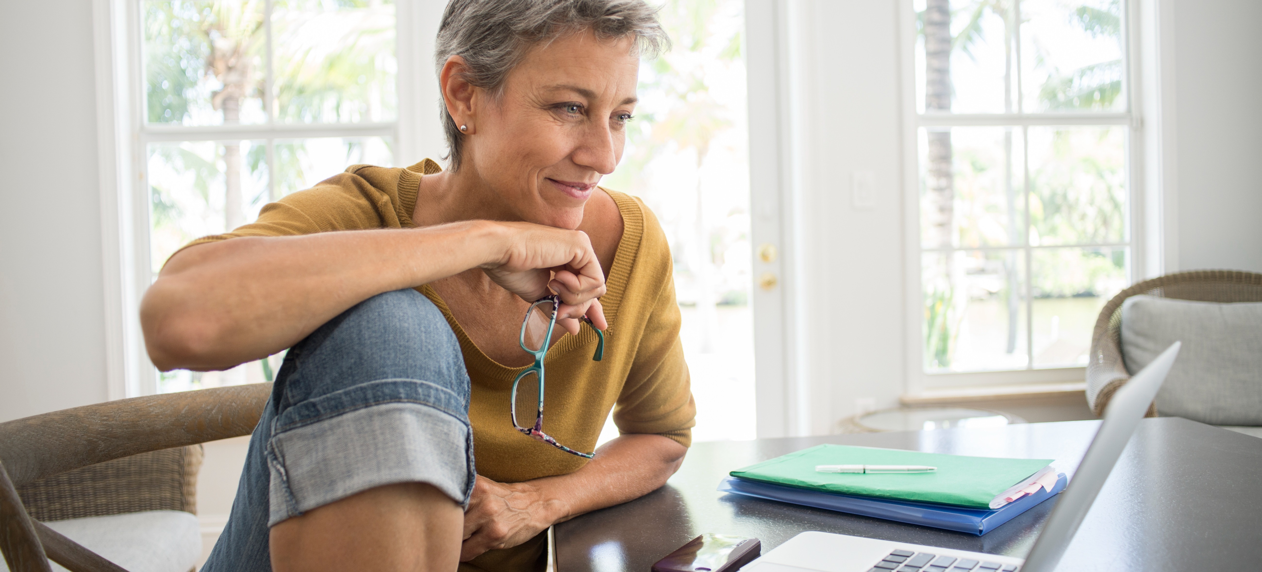 [Featured Image] A woman sits at a laptop in her home and researches how to write a resignation letter. 
