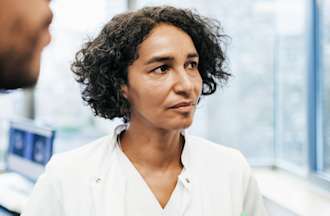 [Featured Image] A woman in a white medical coat stands in a clinic. 