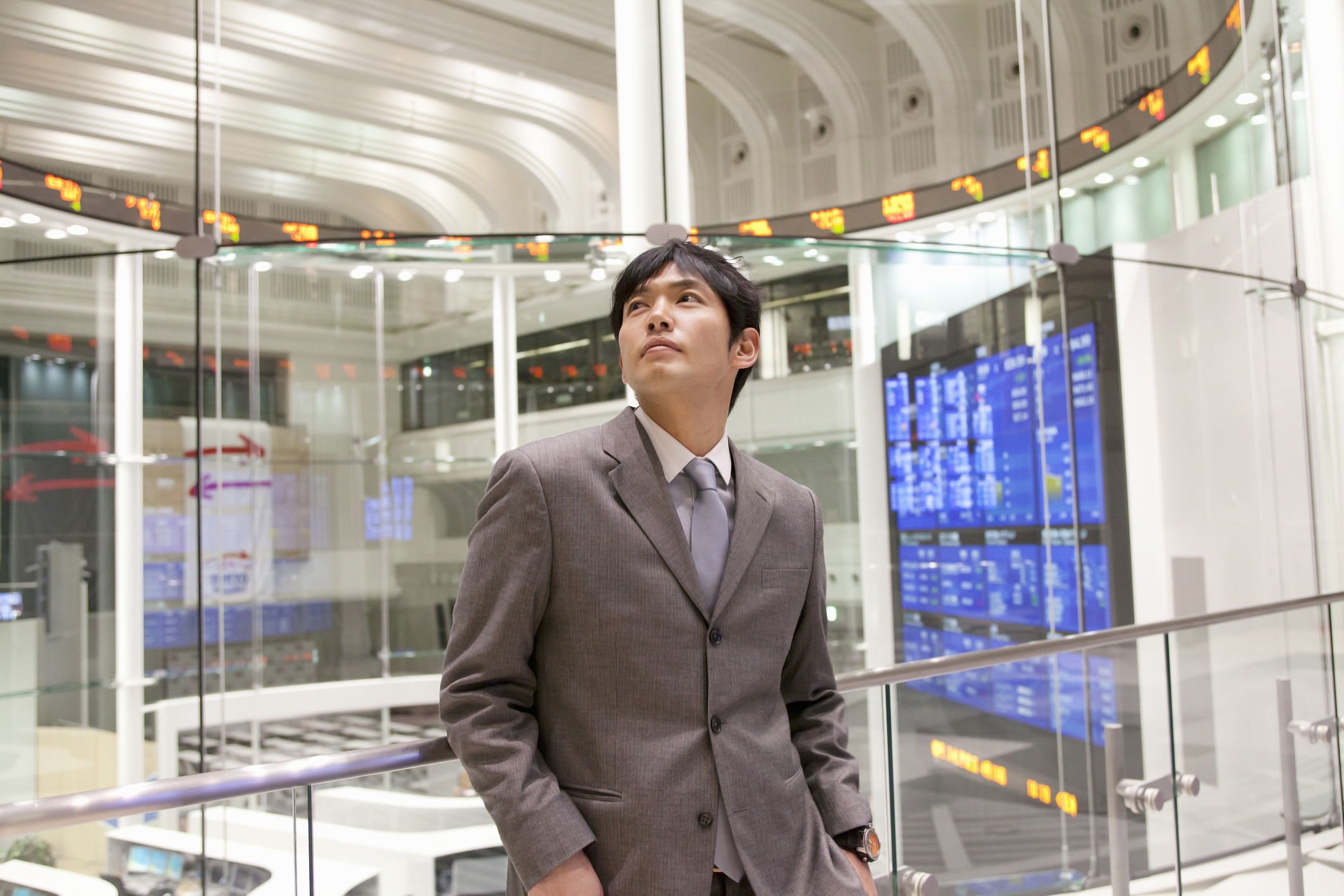 [Featured Image] Un homme d'affaires se tient à la bourse de Toyko et regarde de nombreux affichages d'actions, qui sont analysés à l'aide de statistiques descriptives.