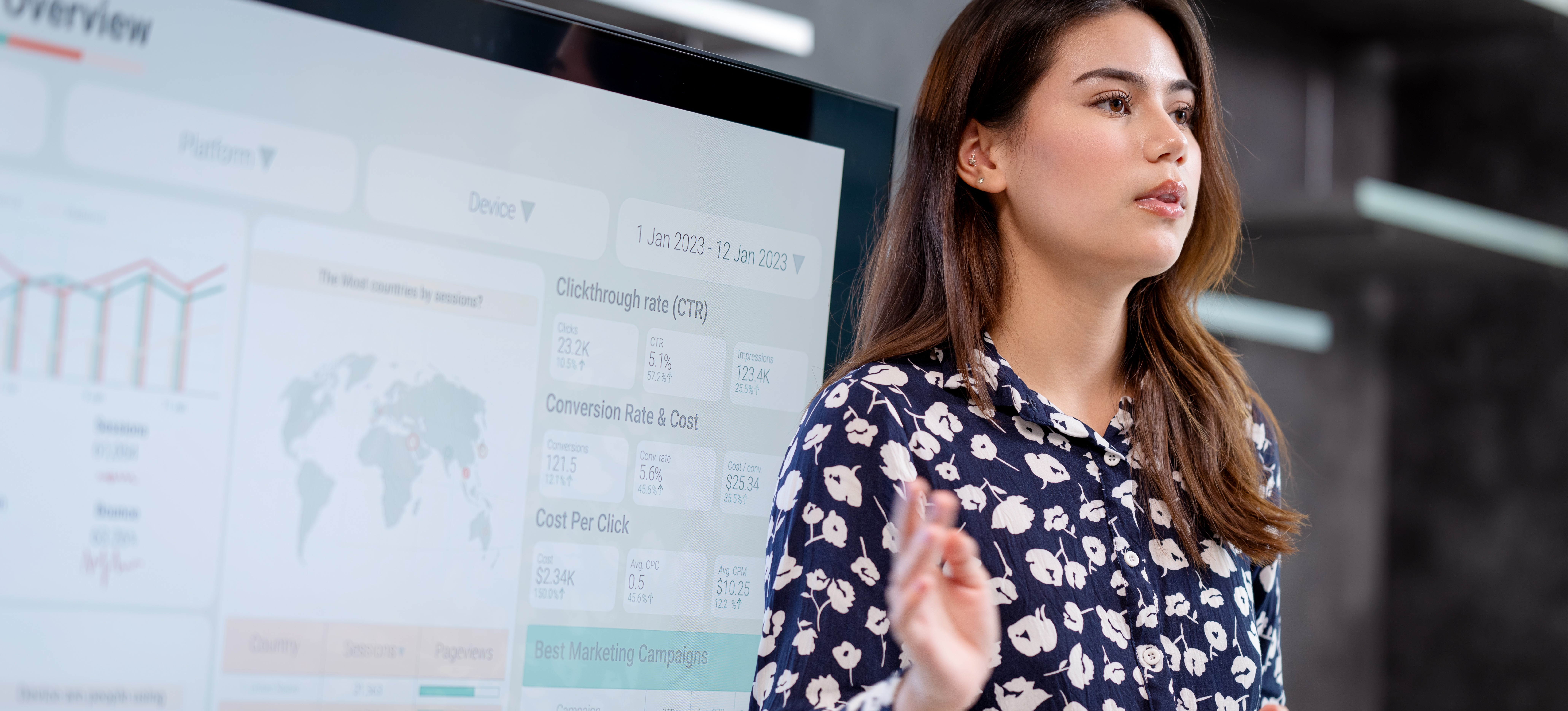 [Featured Image] A sales data analyst stands in front of a screen and presents sales data to her colleagues during a meeting. 
