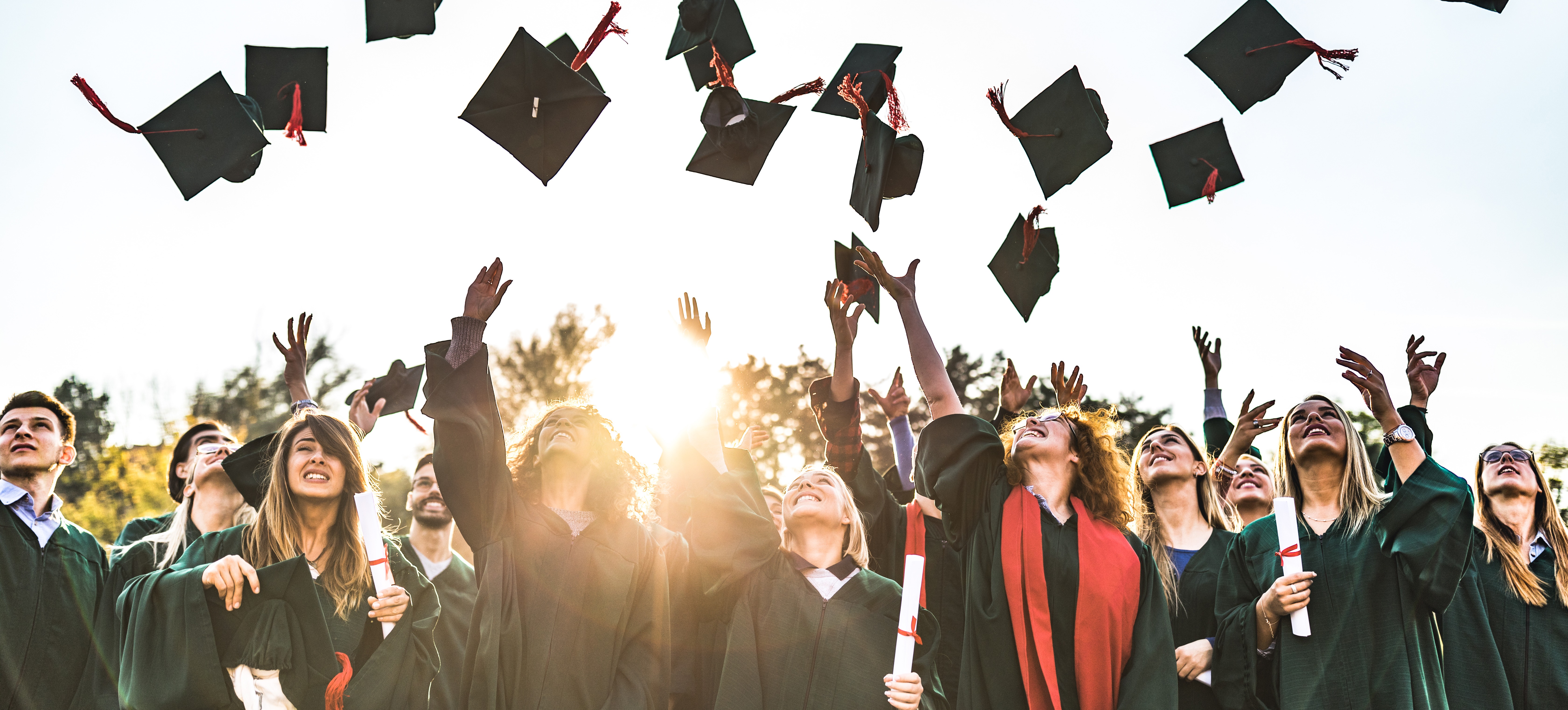 [Featured Image] College students smiling in their graduation gowns and tossing their caps in the air after choosing the right degree and graduating successfully. 
