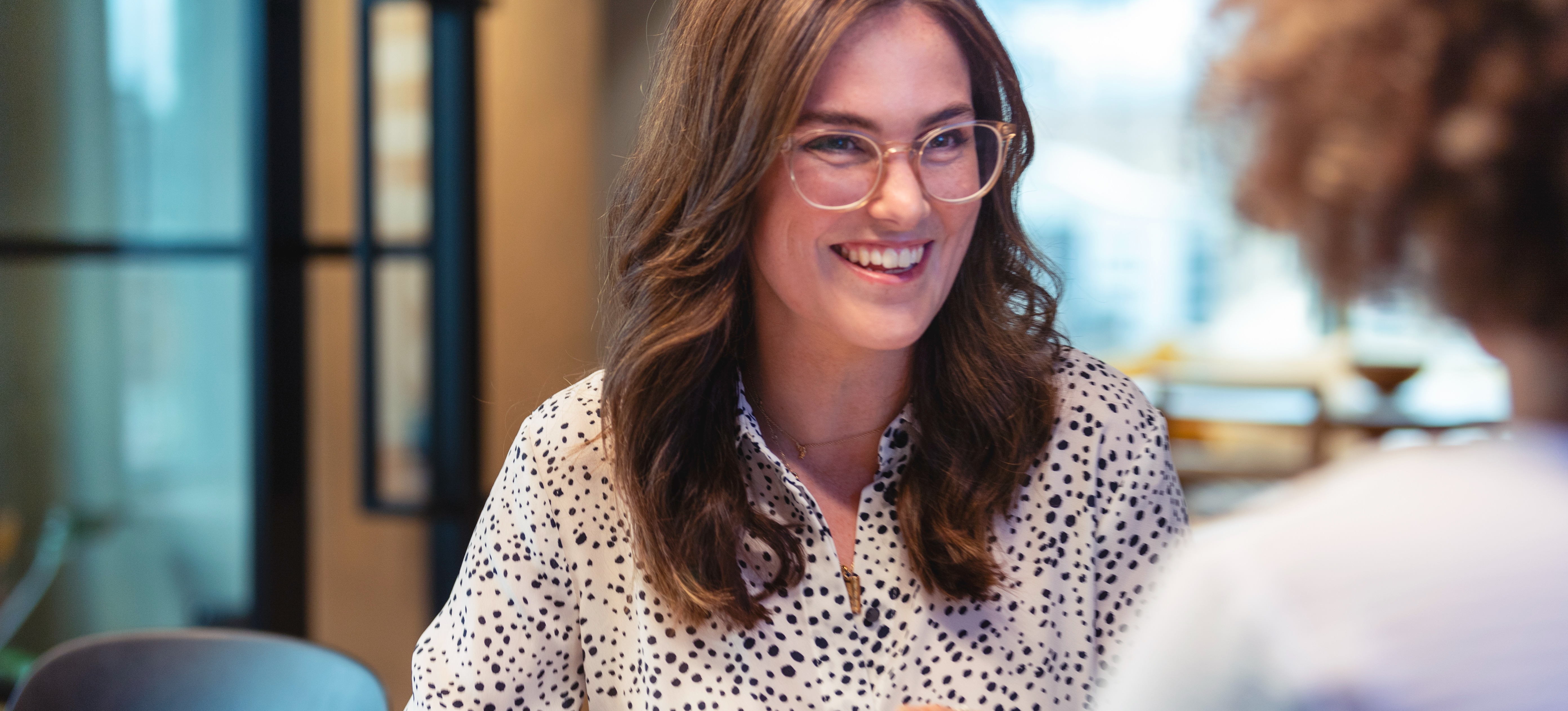 [Featured Image] An employee wearing glasses smiles at her supervisor as she listens to feedback during her annual review.

