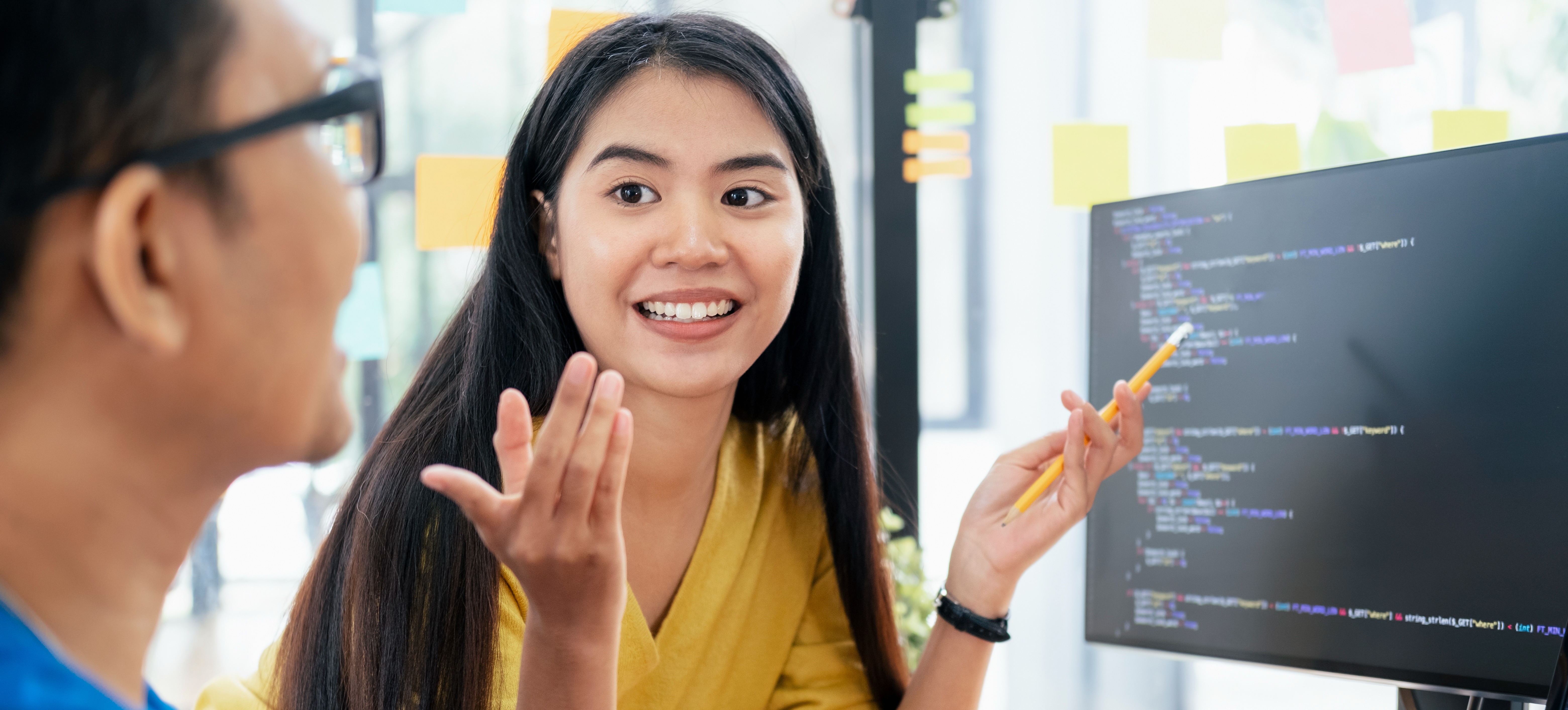 [Featured Image] HTML specialists in a workspace, interacting while reviewing HTML code on a computer and discussing the topic.
