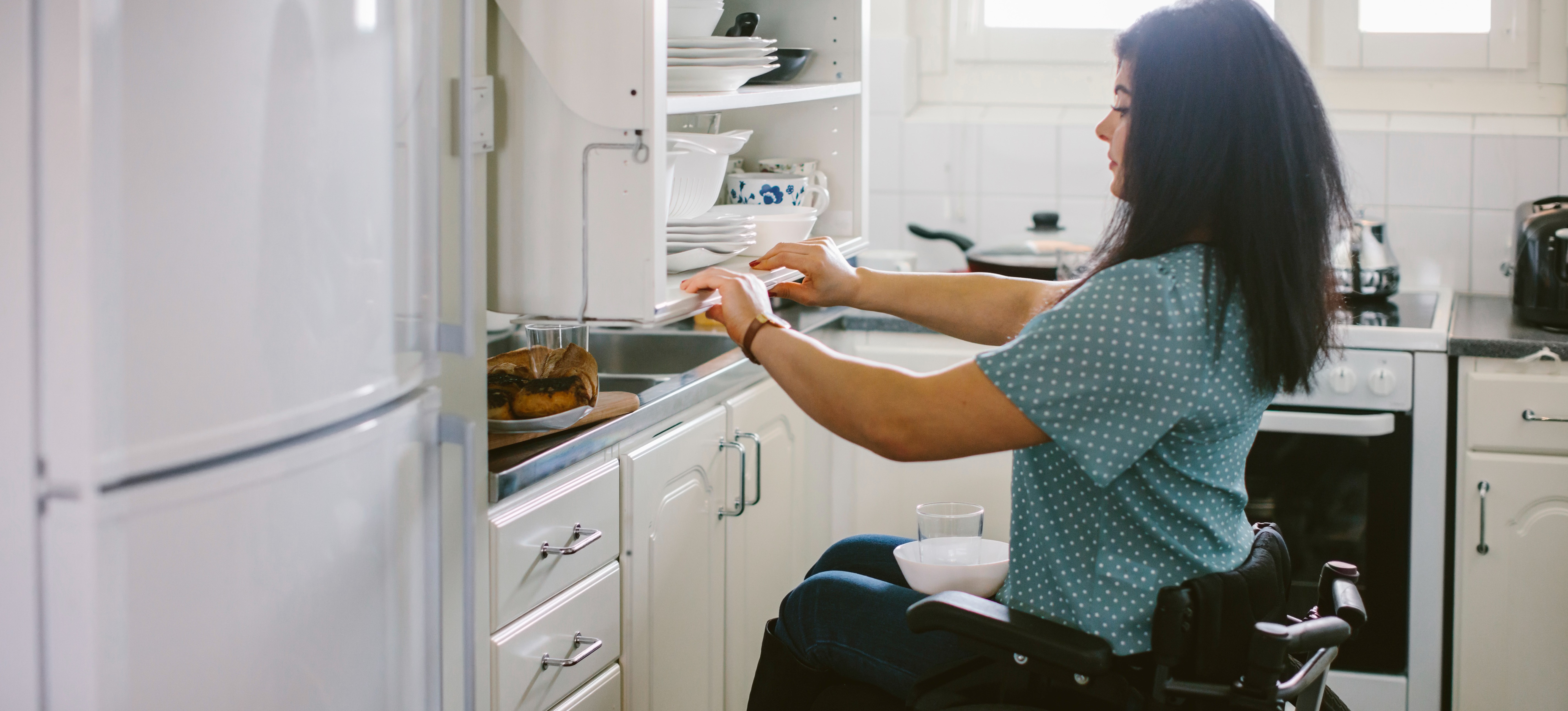 [Featured Image] A young women in a wheel chair uses assistive technology in her home.