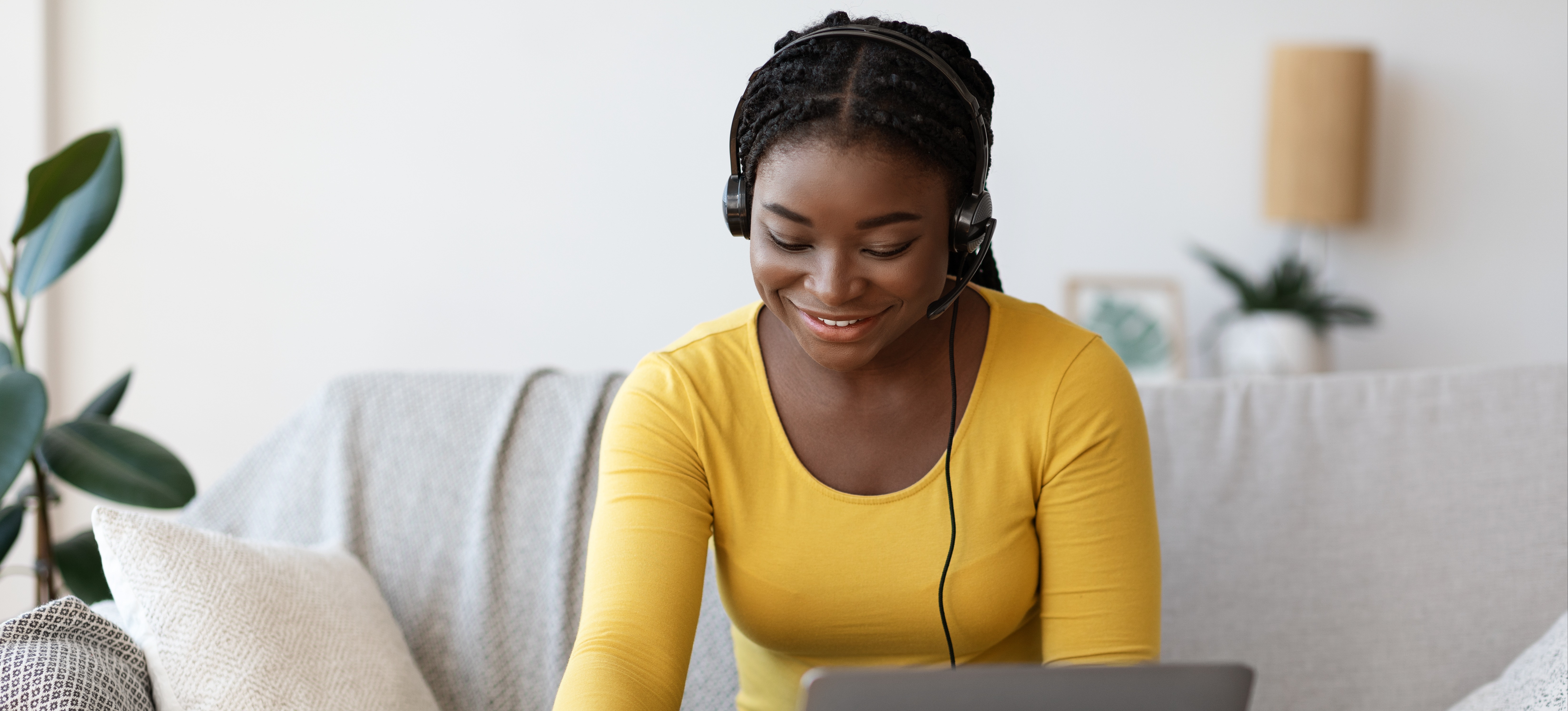 [Feature Image] A learner in a yellow top and blue jeans sits on a neutral-colored couch and uses a laptop to research, “Is a master’s degree worth it?”