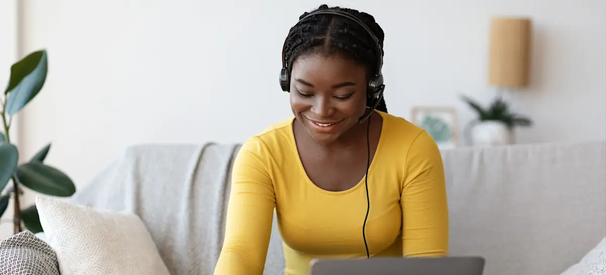[Feature Image] A learner in a yellow top and blue jeans sits on a neutral-colored couch and uses a laptop to research, “Is a master’s degree worth it?”