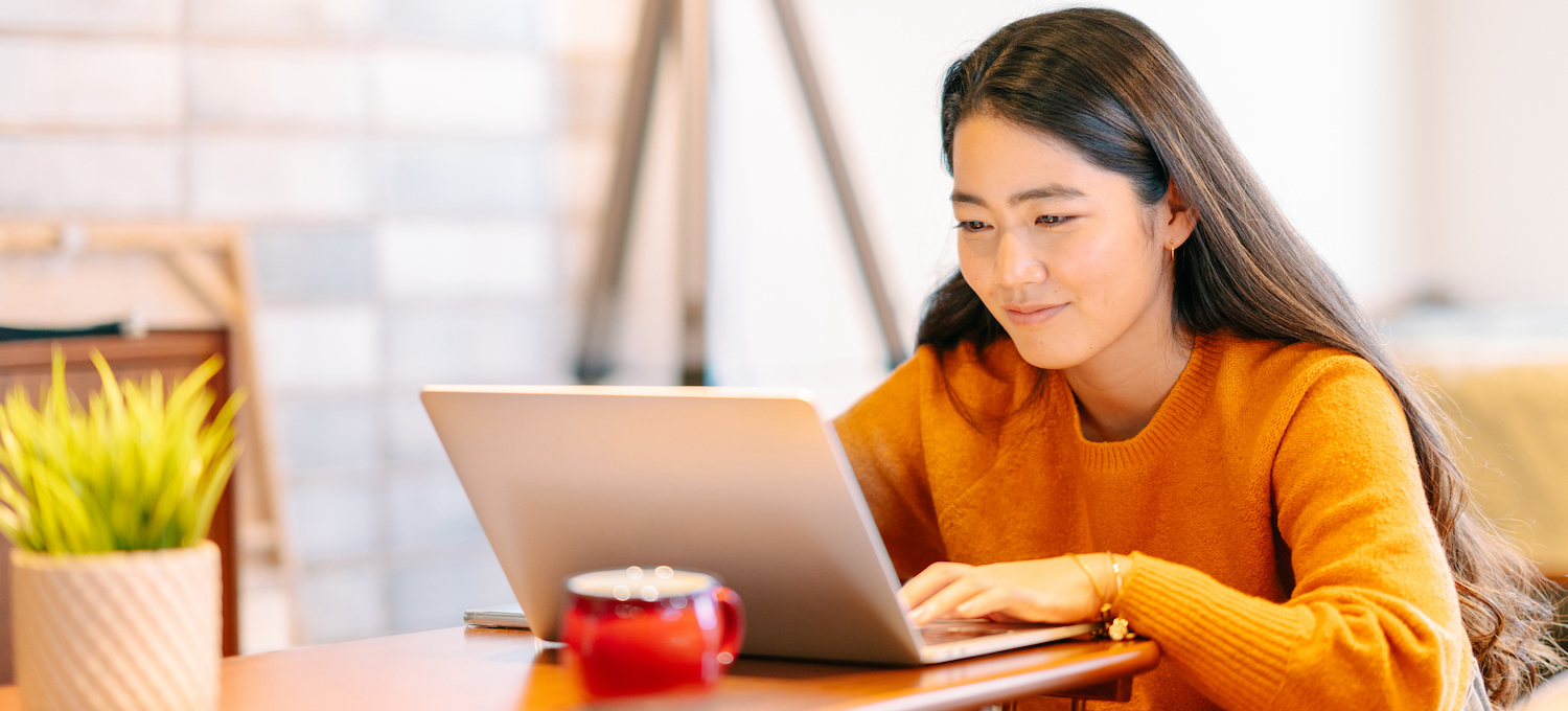 [Featured image] A smiling person wearing an orange sweater looks at their laptop. 