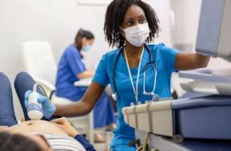 [Featured Image] A sonographer wearing blue scrubs performs an ultrasound on a patient. 