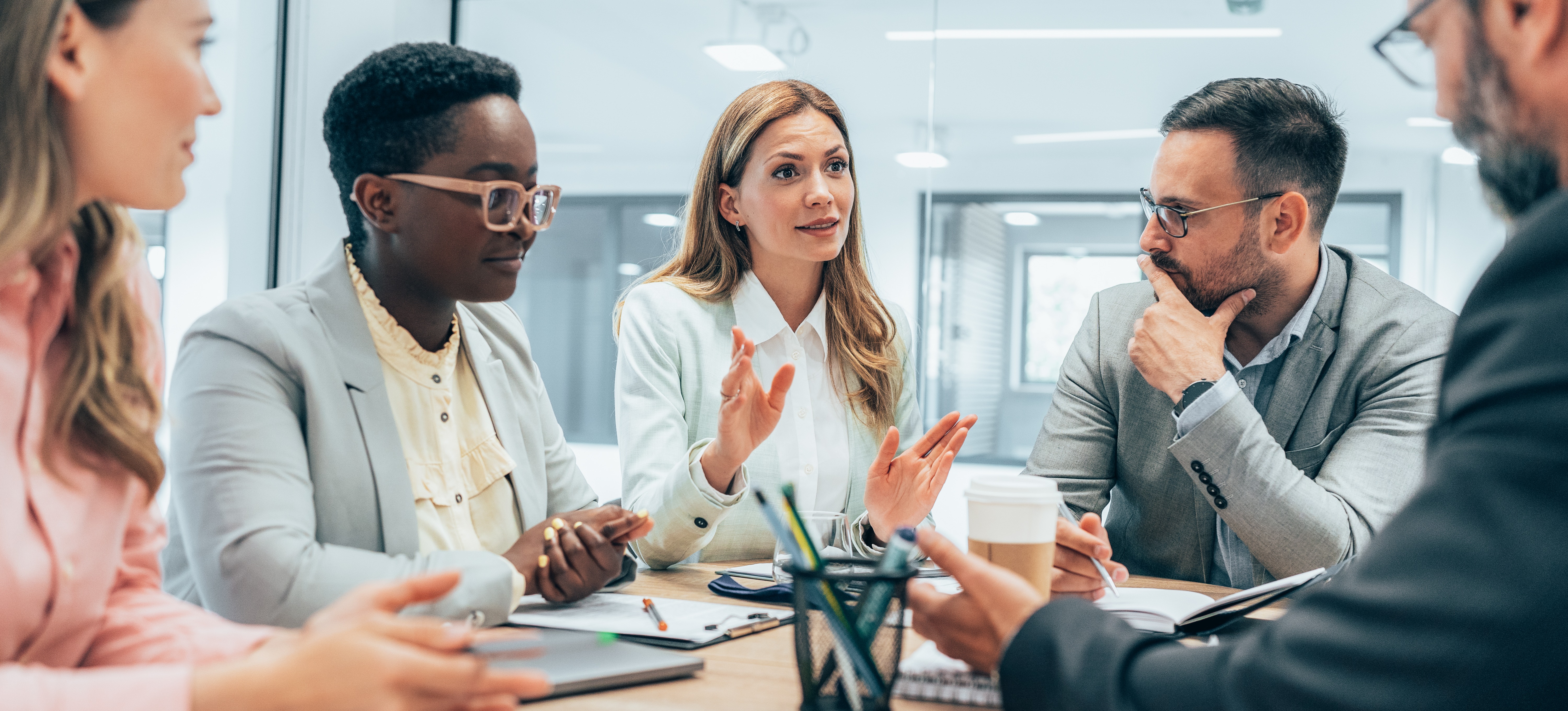 [Image en vedette] Une femme d'affaires utilise ses compétences en matière de gestion de projet pour s'adresser à quatre autres membres de l'équipe lors d'une réunion d'affaires.
