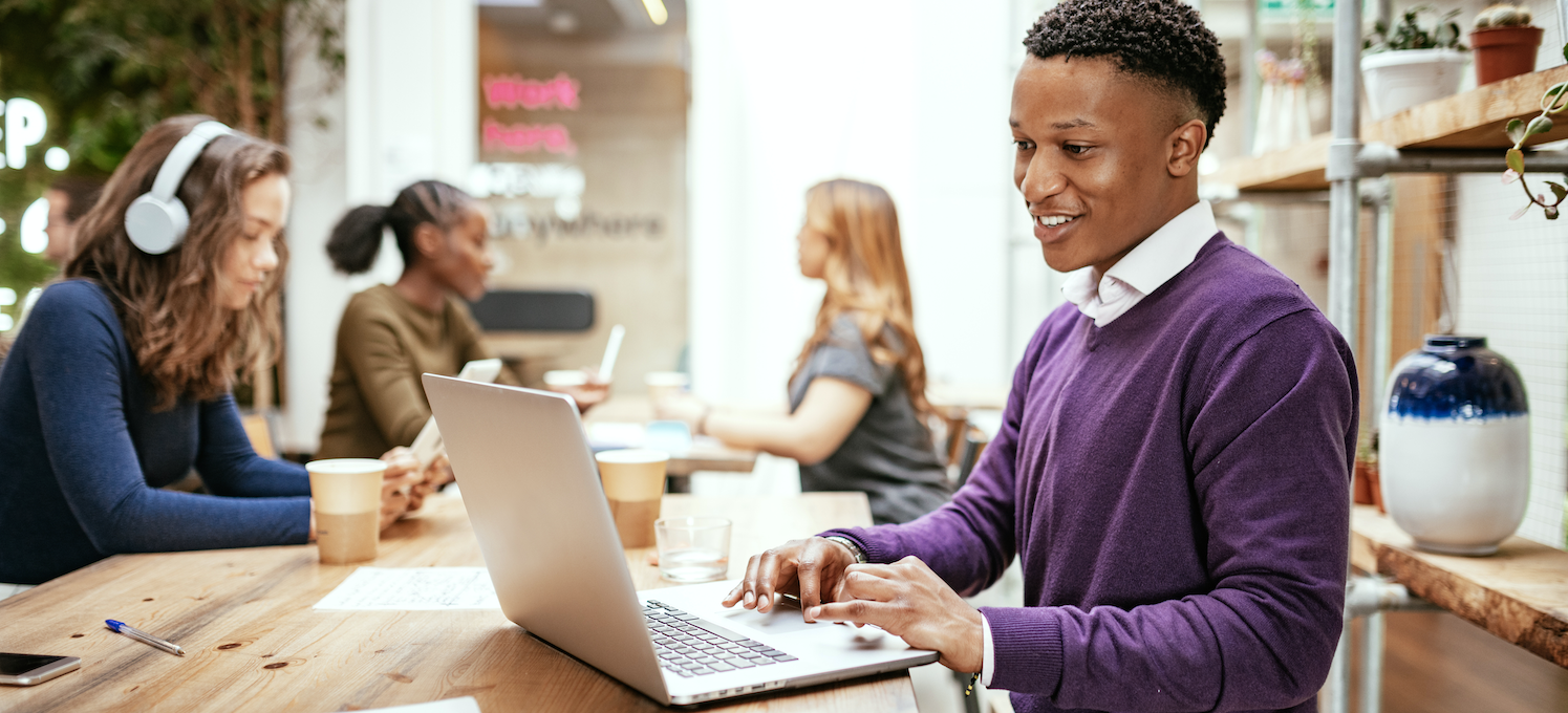 [Featured image] A cloud security engineer wears a purple sweater and works on their laptop at a coffee shop.
