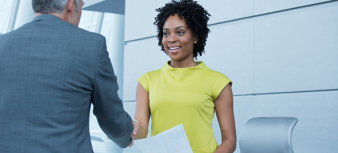 [Featured Image] A job candidate who is prepared with how to answer salary expectations stands and shakes the hand of their interviewer after being offered the job.
