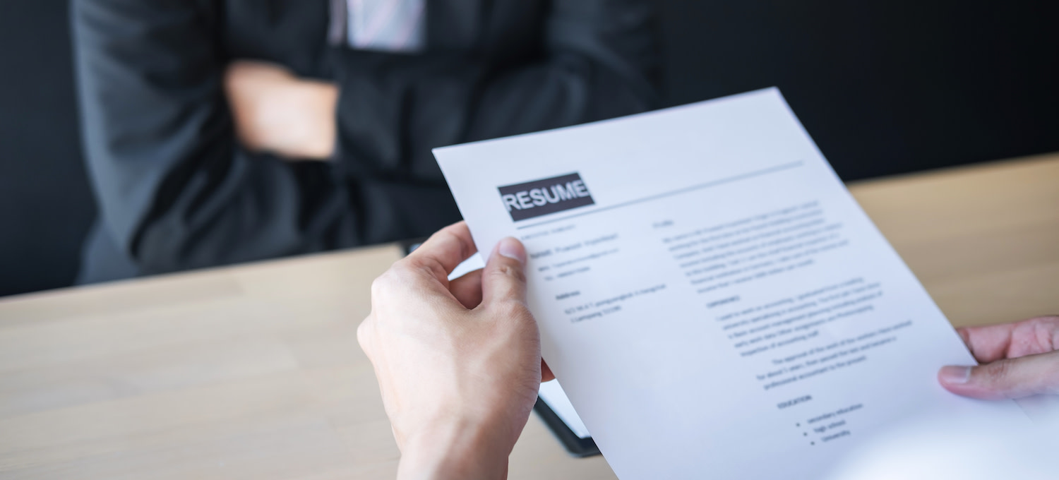[Featured image] An abstract image showing a person's hands holding a resume while a person in a suit sits in front of them. 