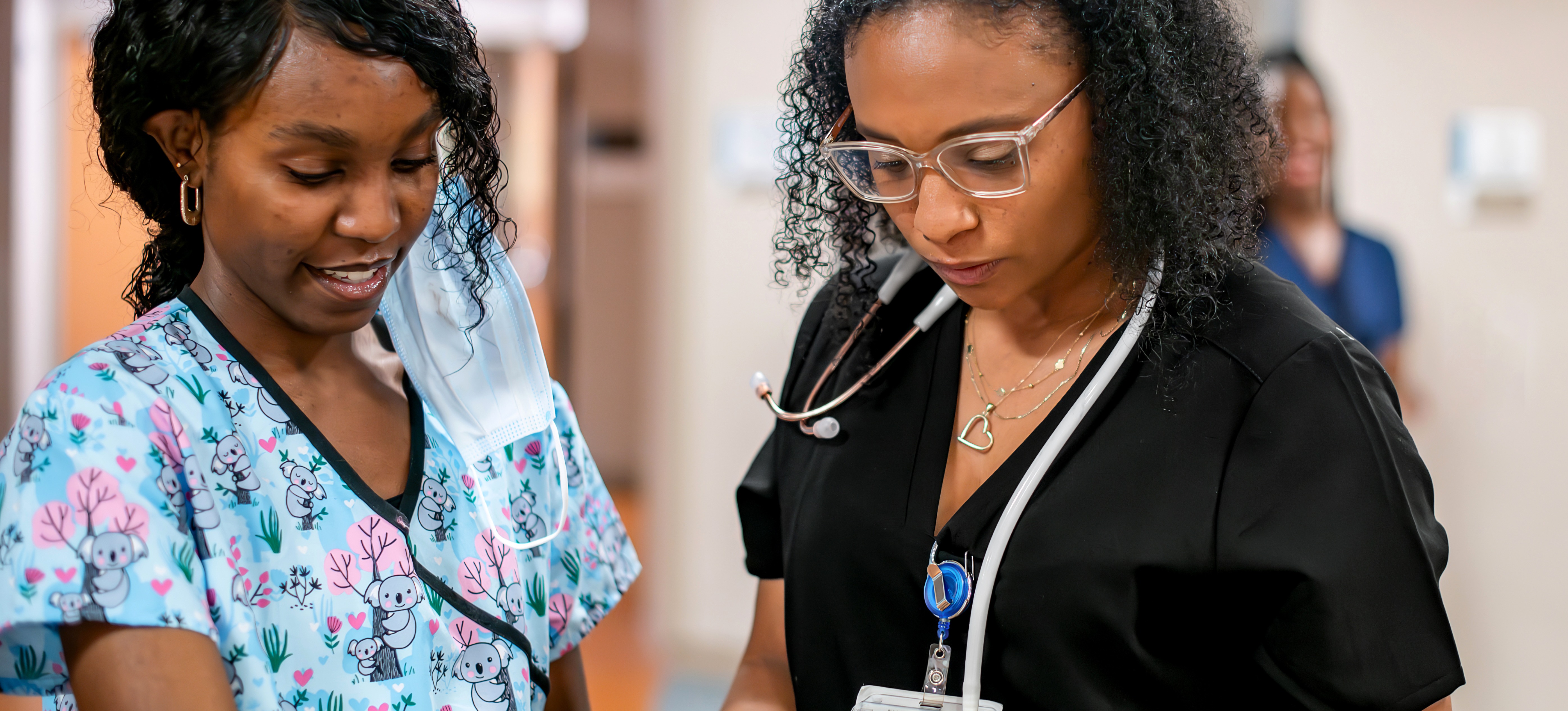 [Featured Image] Two nurses exhibiting the nursing skills of collaboration and patient care as they read over a chart together. 

