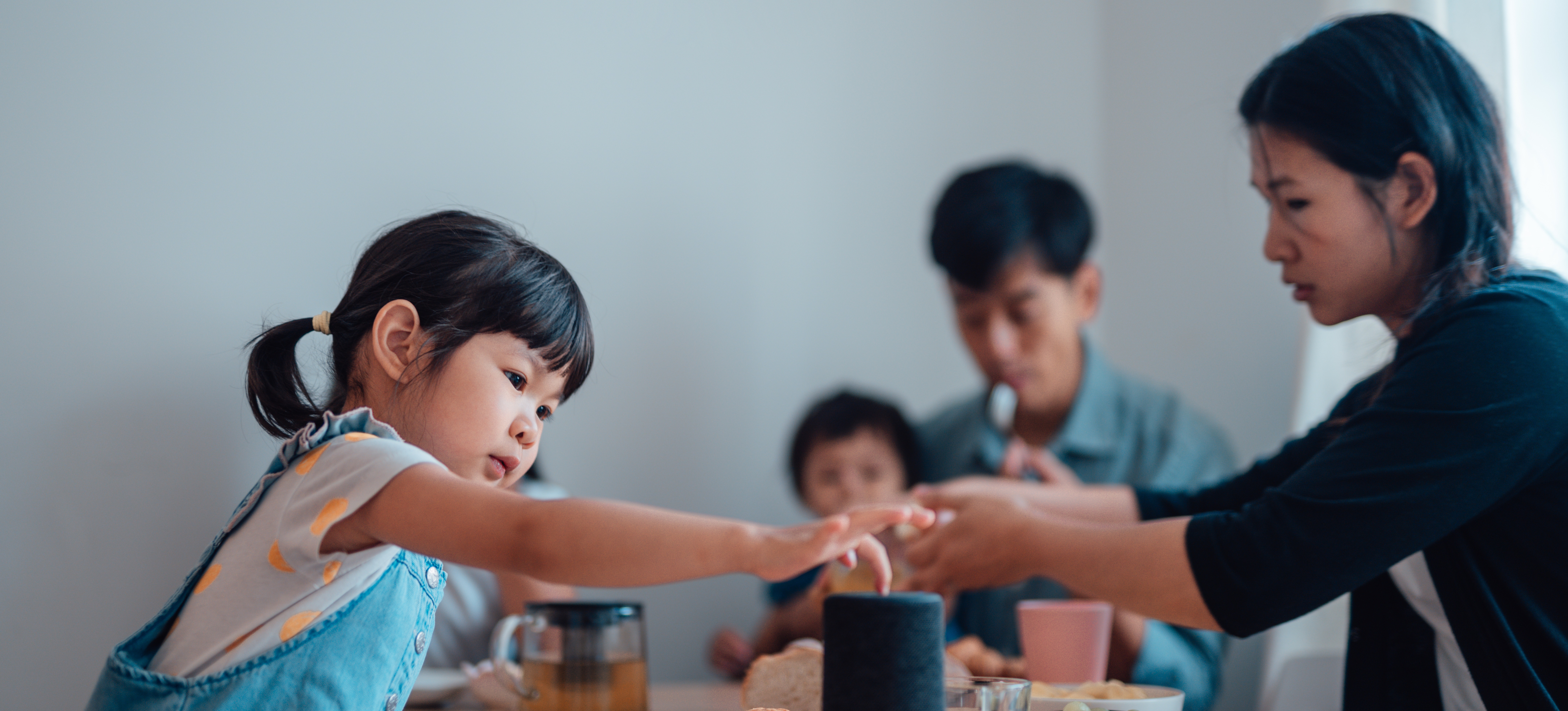 [Featured Image] A young family of four sits at a dining table as one child uses a virtual assistant, one of many deep learning examples you may use daily.
