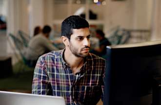 [Featured image] A software developer is sitting at their desk in front of a desktop and a laptop.