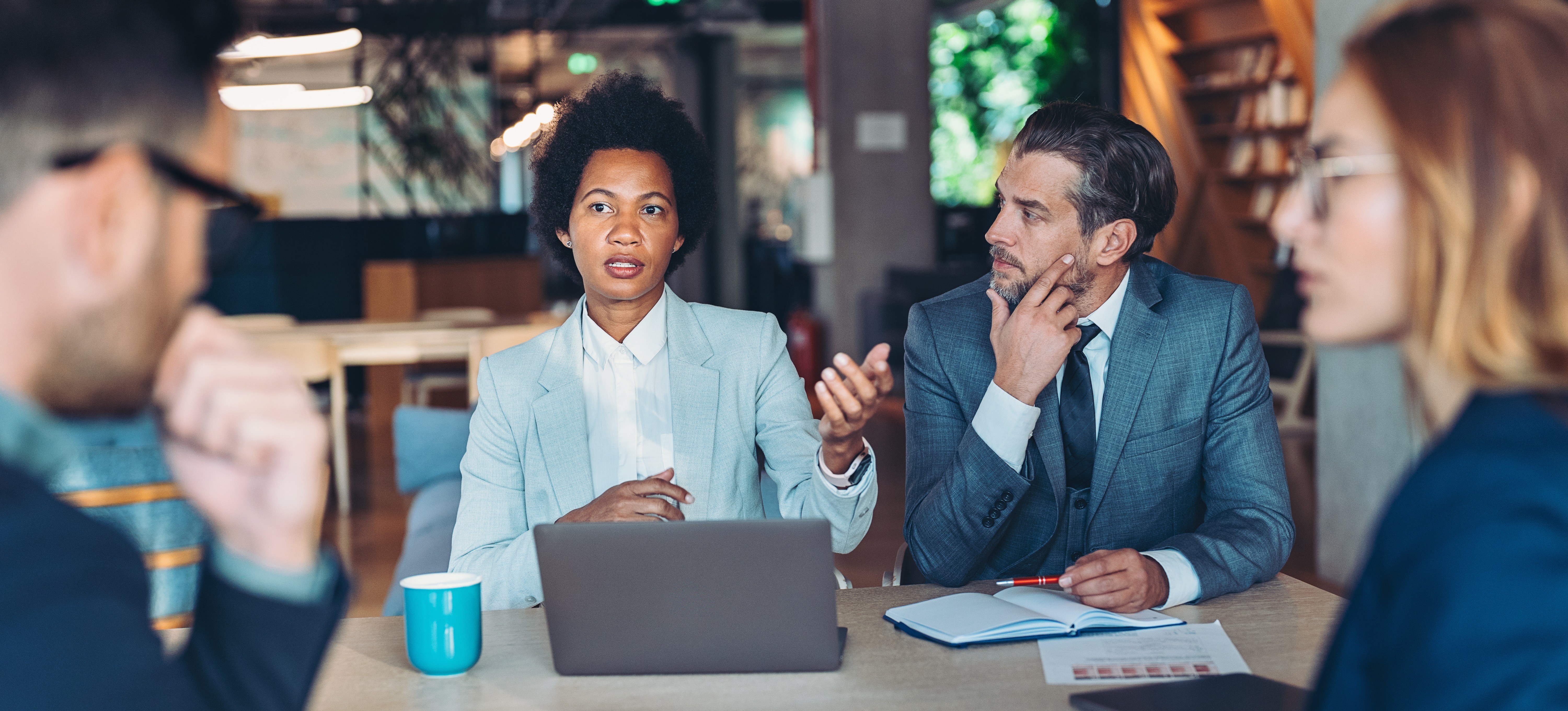 [Featured Image] A team of three sit at a table and discuss with the cpim of their company.