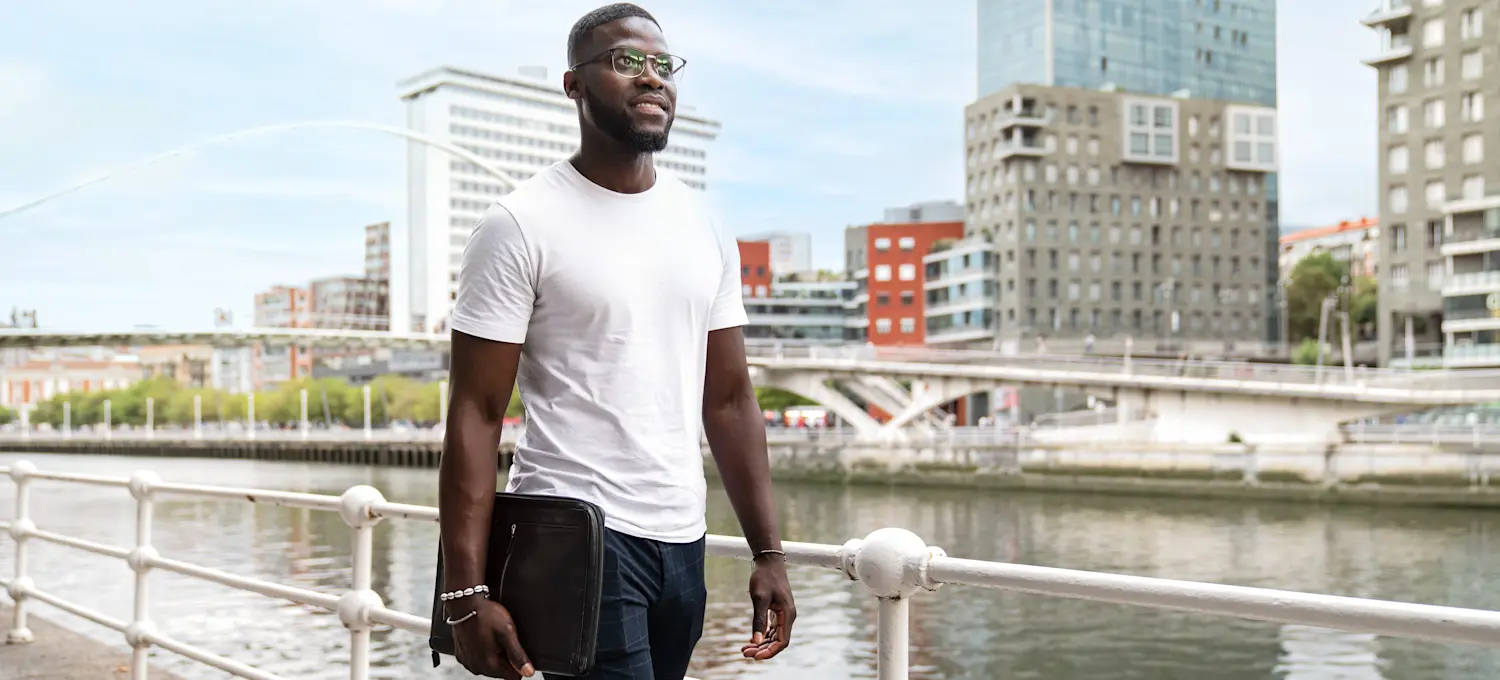 [Featured Image] A confident casual businessperson walking near the harbor and looking straight ahead while they are thinking about getting a master's degree.