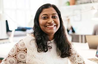 A smiling woman in a white lace shirt sits in front of a laptop with user research data on the screen