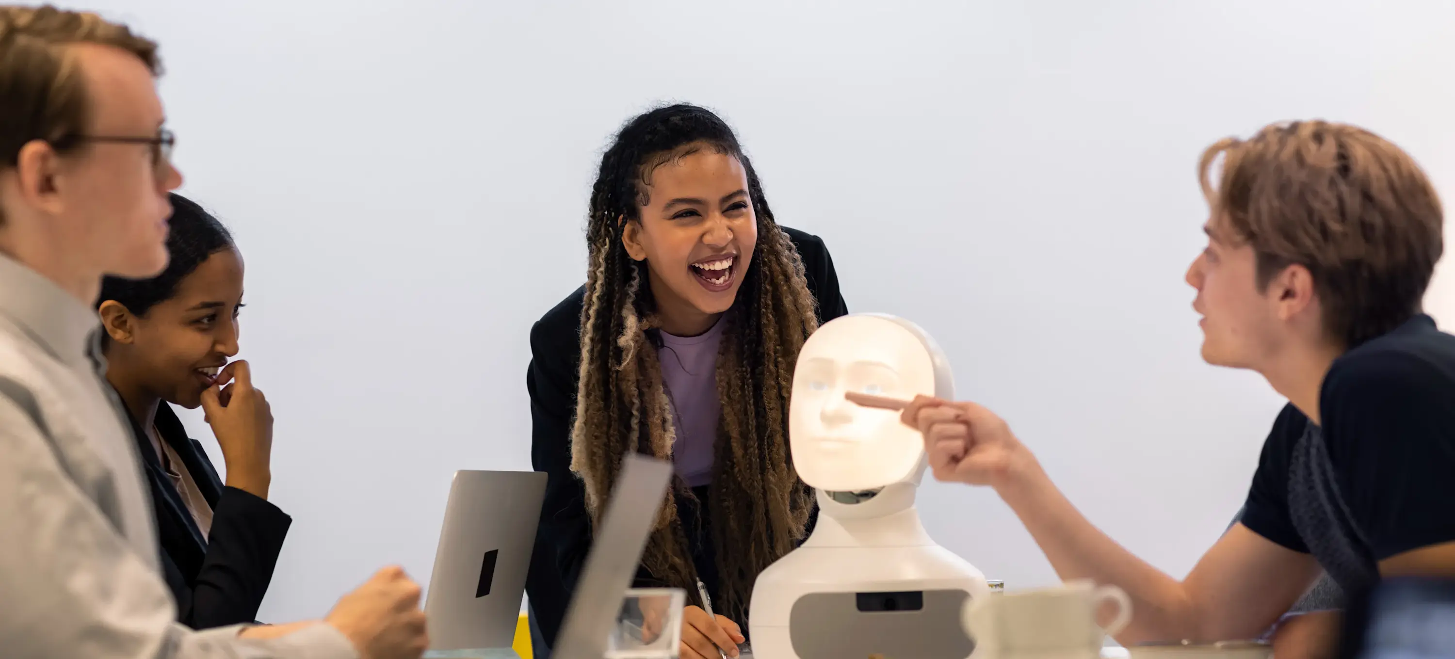 [Featured Image] A group of four machine learning engineers is discussing a robotic device. One person is standing at the head of the table and laughing, while a person next to them is talking while pointing to the robotic device with a pencil. The other two people appear to be listening.

