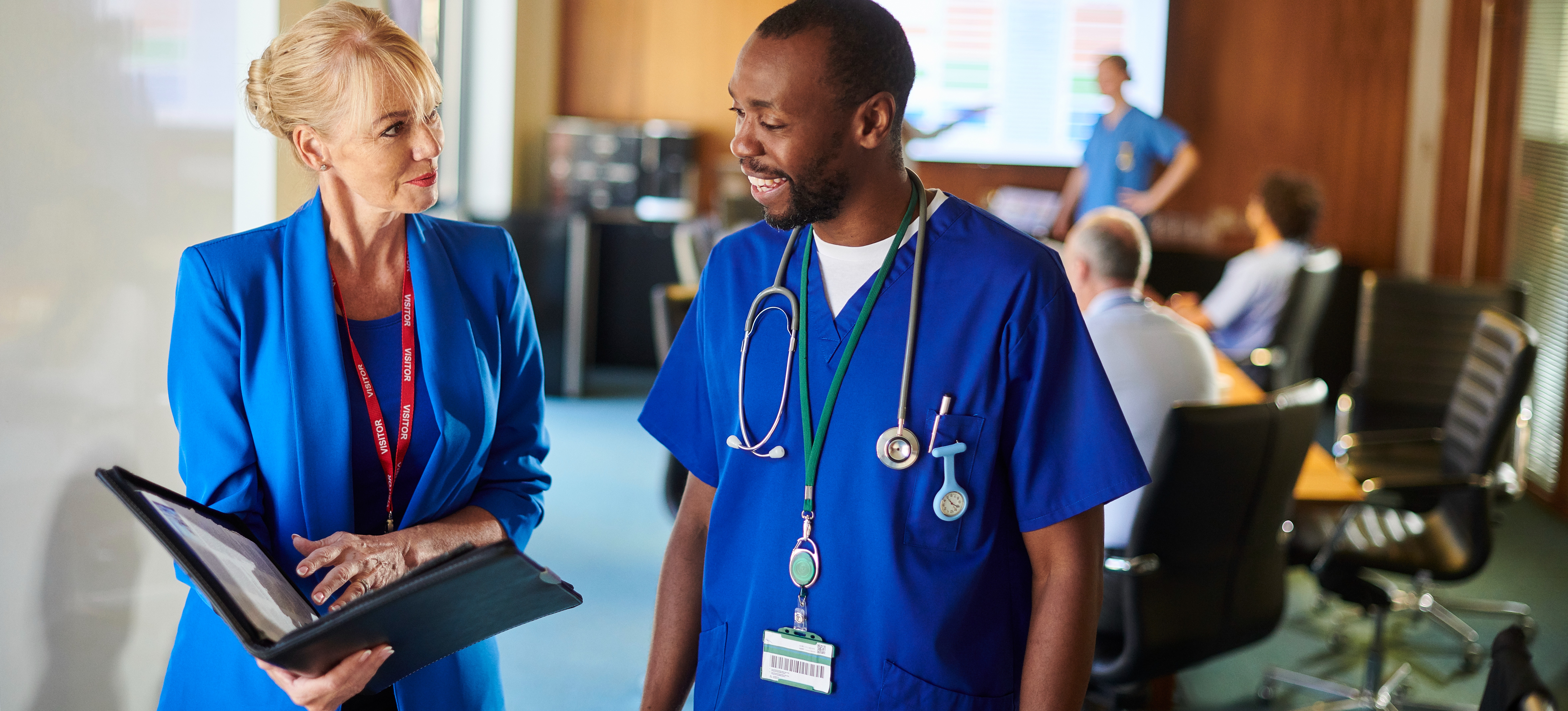 [Featured Image] A hospital administrator stands in a hospital boardroom and talks with a head doctor, both of who have earned health care MBAs.