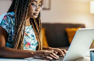 [Featured image] A person in a floral shirt with braided hair works remotely from home on a laptop computer.