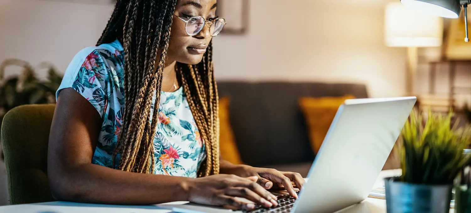[Featured image] A person in a floral shirt with braided hair works remotely from home on a laptop computer.