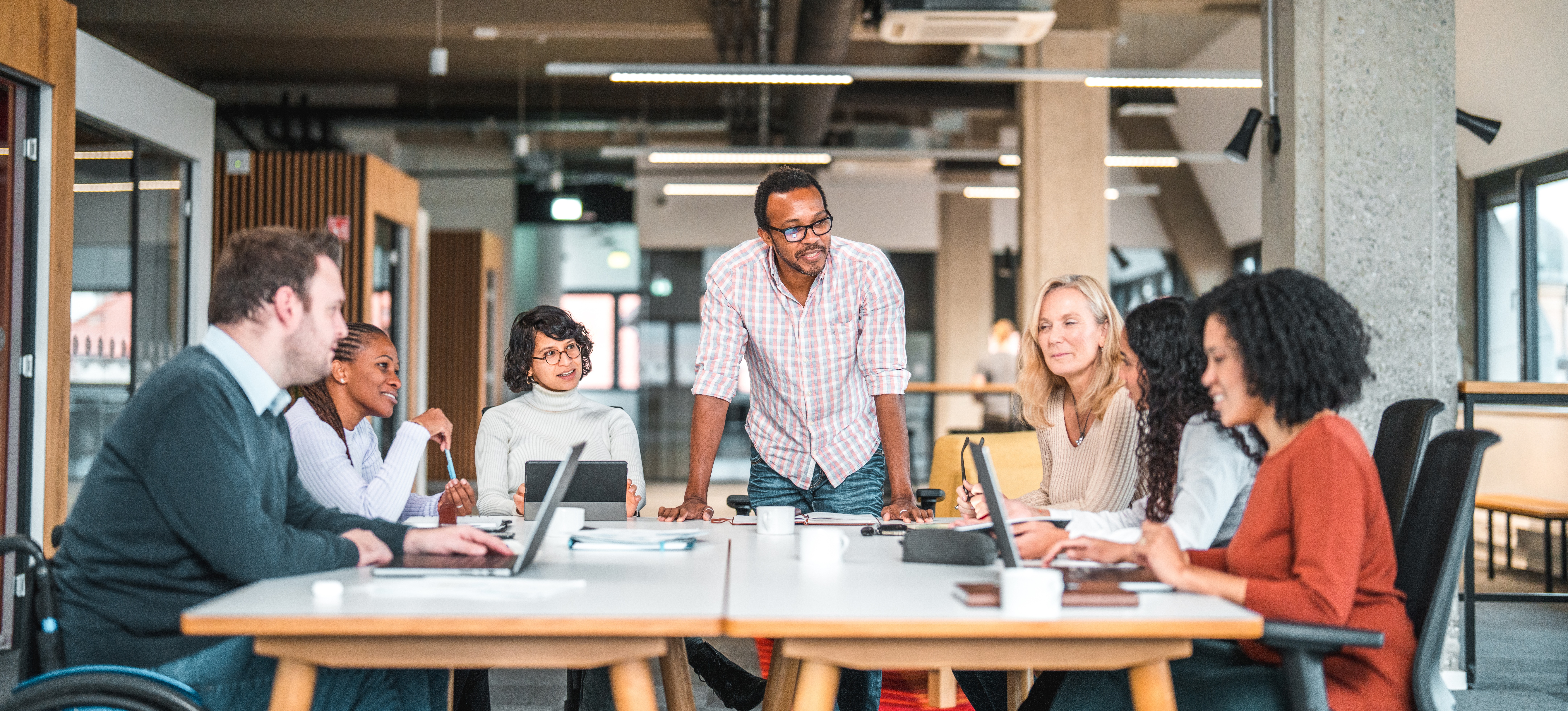 [Hauptbild] Ein Team von Entwicklern, die in einer modernen Büroumgebung um einen großen Tisch sitzen, nutzt Lean UX, um während des UX-Designprozesses zusammenzuarbeiten.
