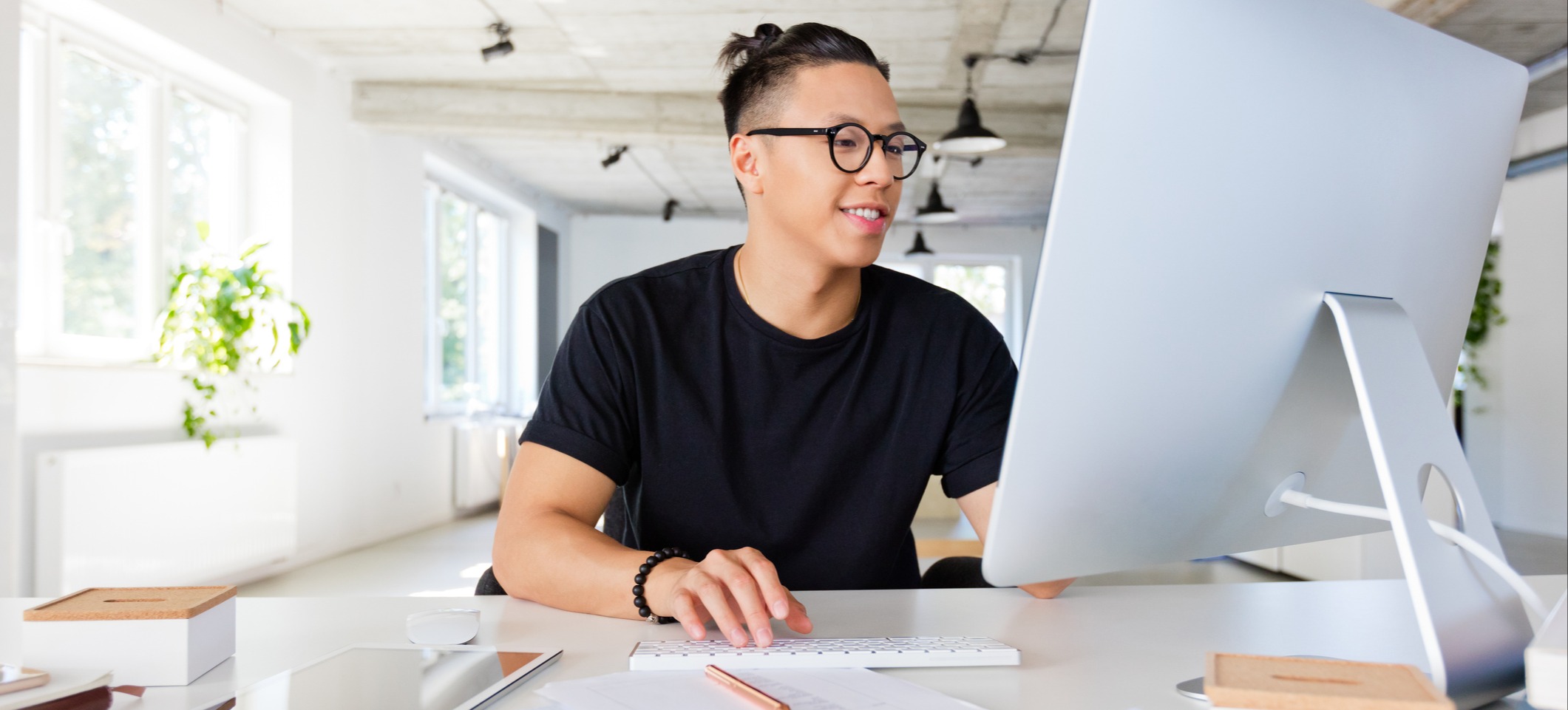 [Featured Image] A person in a black shirt works in an office at a desktop computer. 