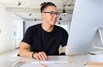 [Featured Image] A man in a black shirt works in an office at a desktop computer. 