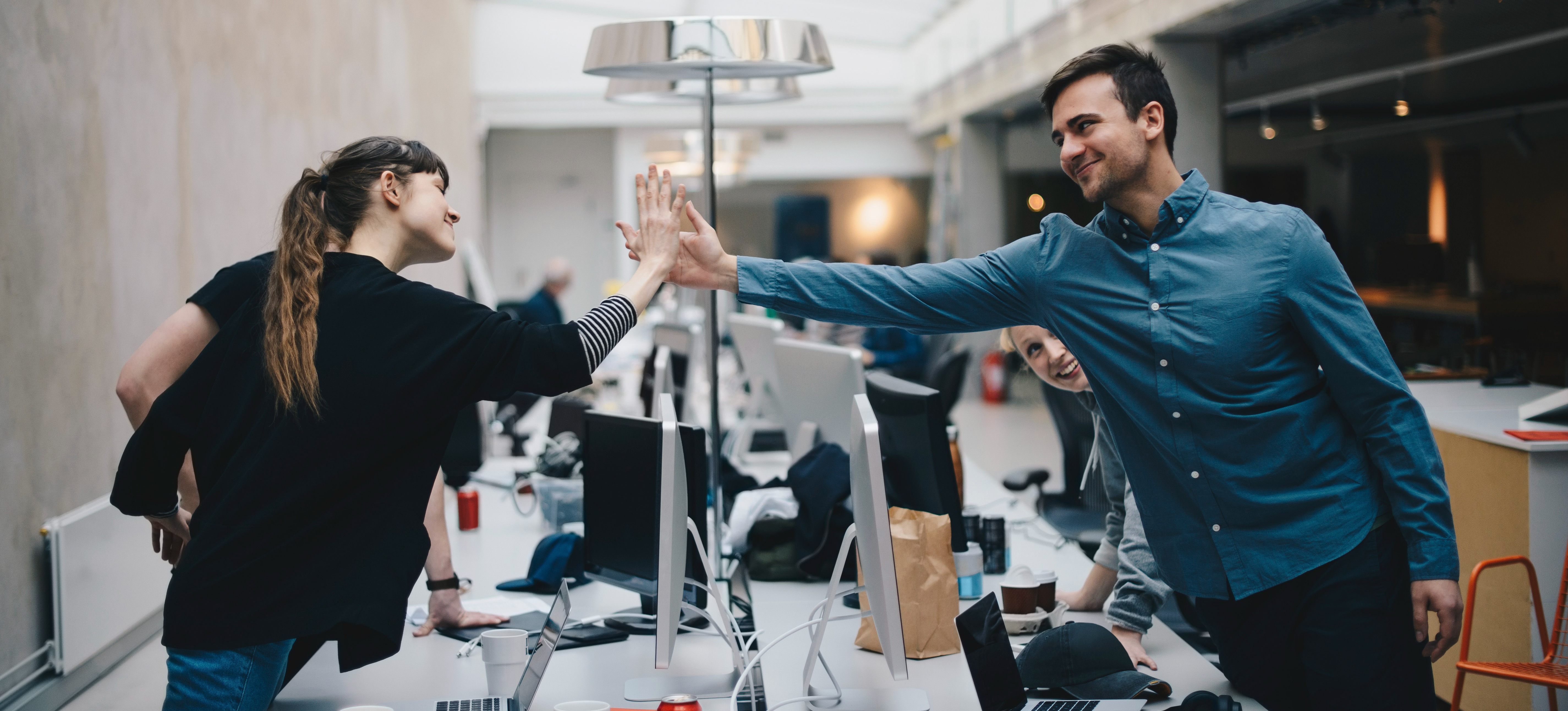 [Featured Image] A quality assurance engineer is high fiving his team member during a break from their project.