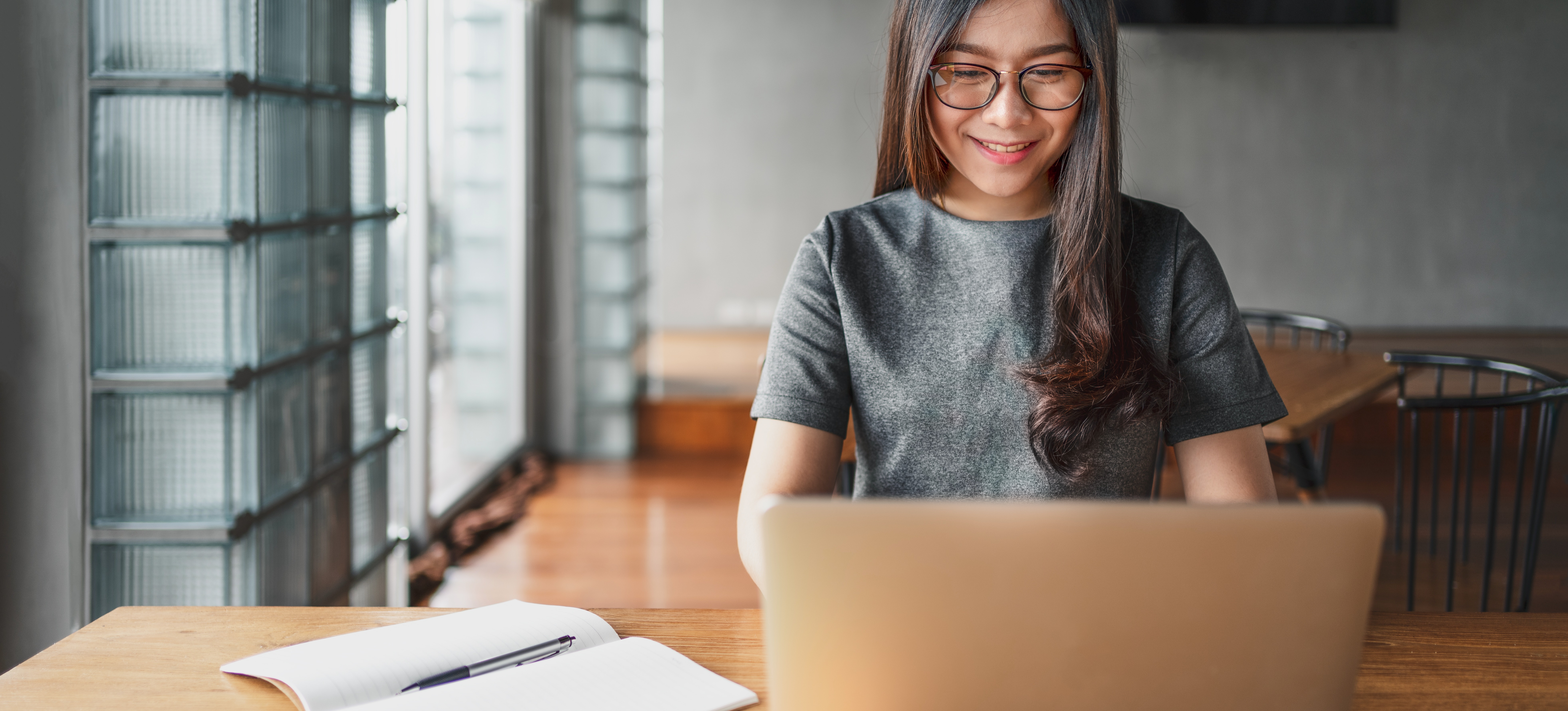 [Featured Image] A college student sits at a table in a library, typing her resume on a laptop.
