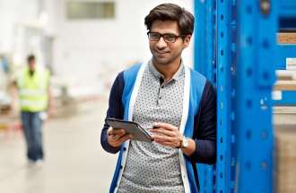 [Featured Image] A supply chain manager stands in a warehouse holding a tablet.