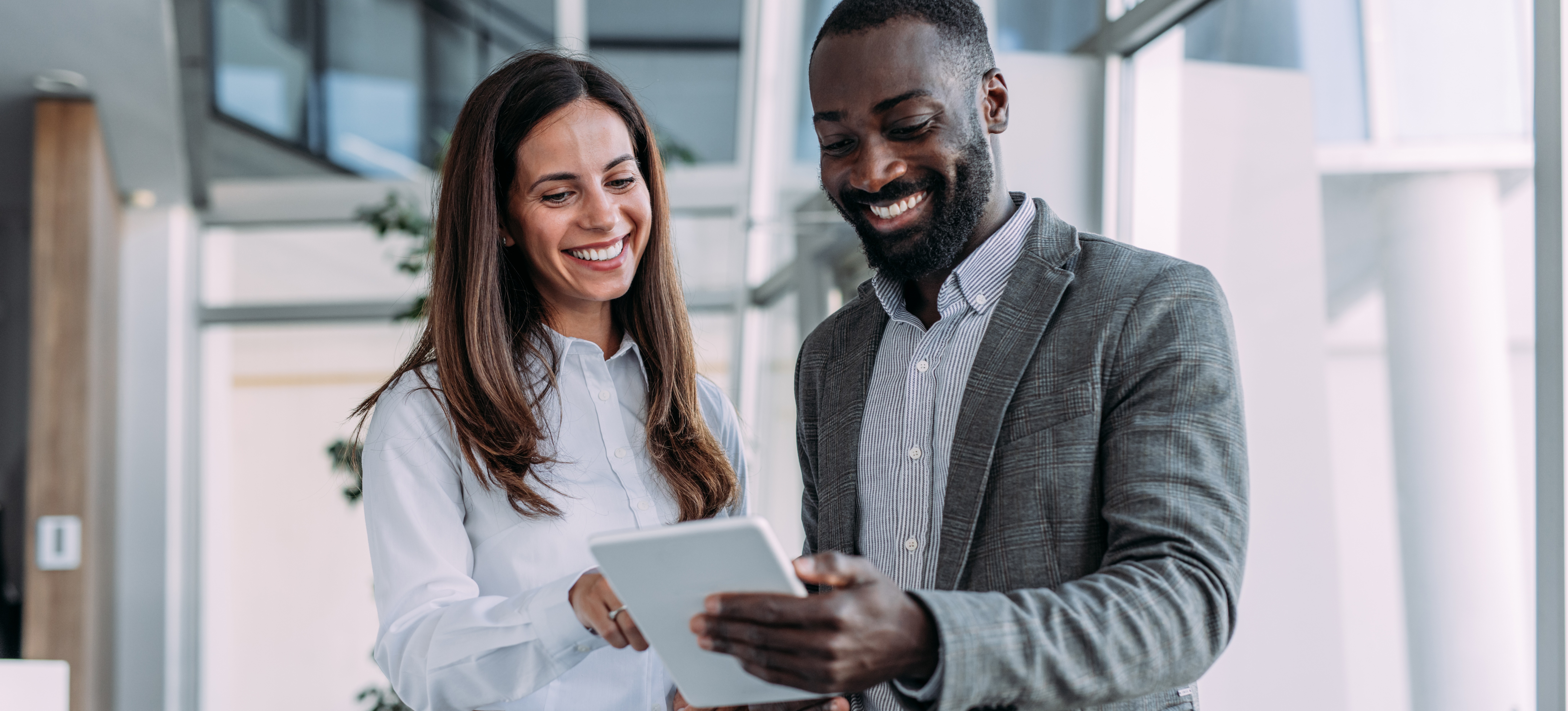 [Hauptbild] Zwei Kollegen lächeln, während sie auf ein Tablet schauen und effektiv miteinander kommunizieren – eine der gefragtesten Kompetenzen.