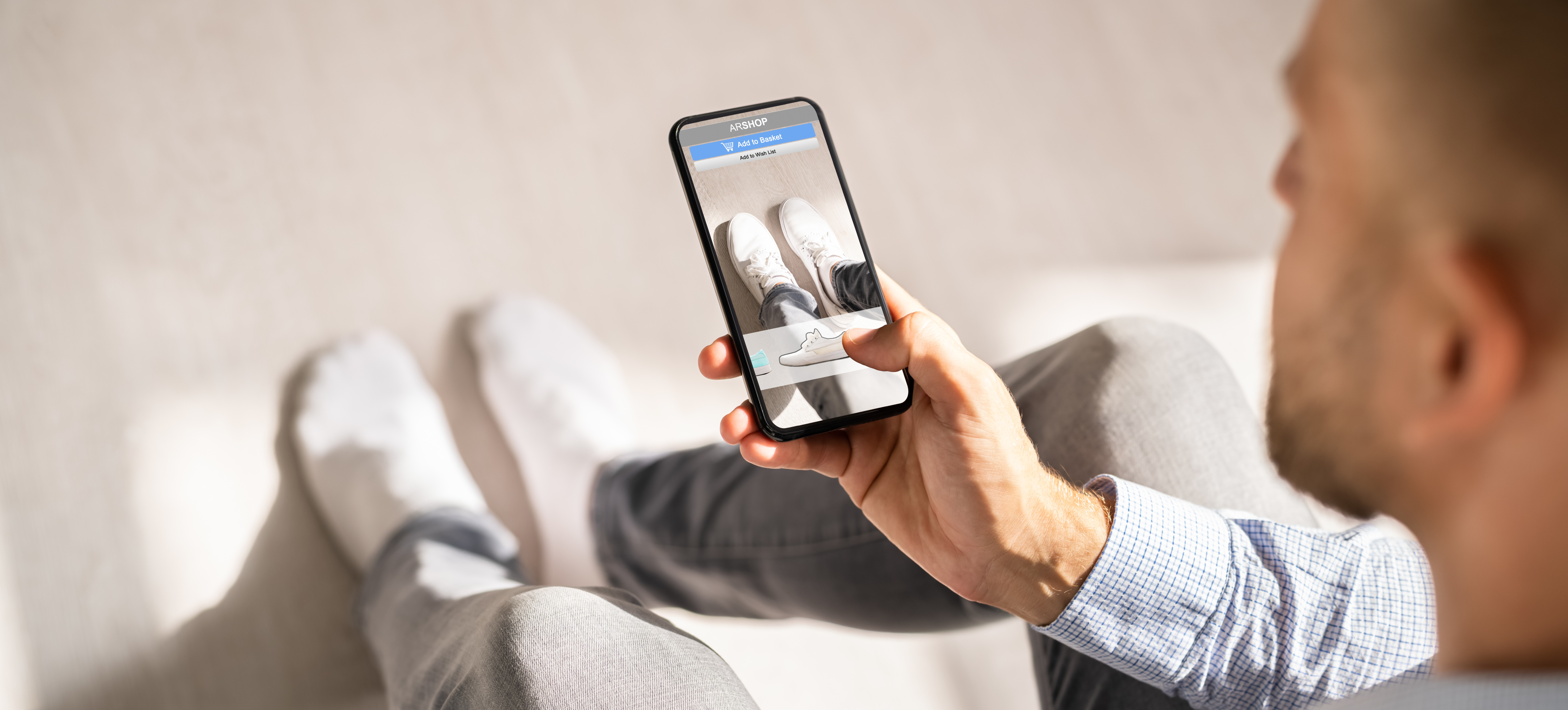 [Featured Image] A consumer with a smartphone uses augmented reality advertising to try on a pair of tennis shoes virtually.

