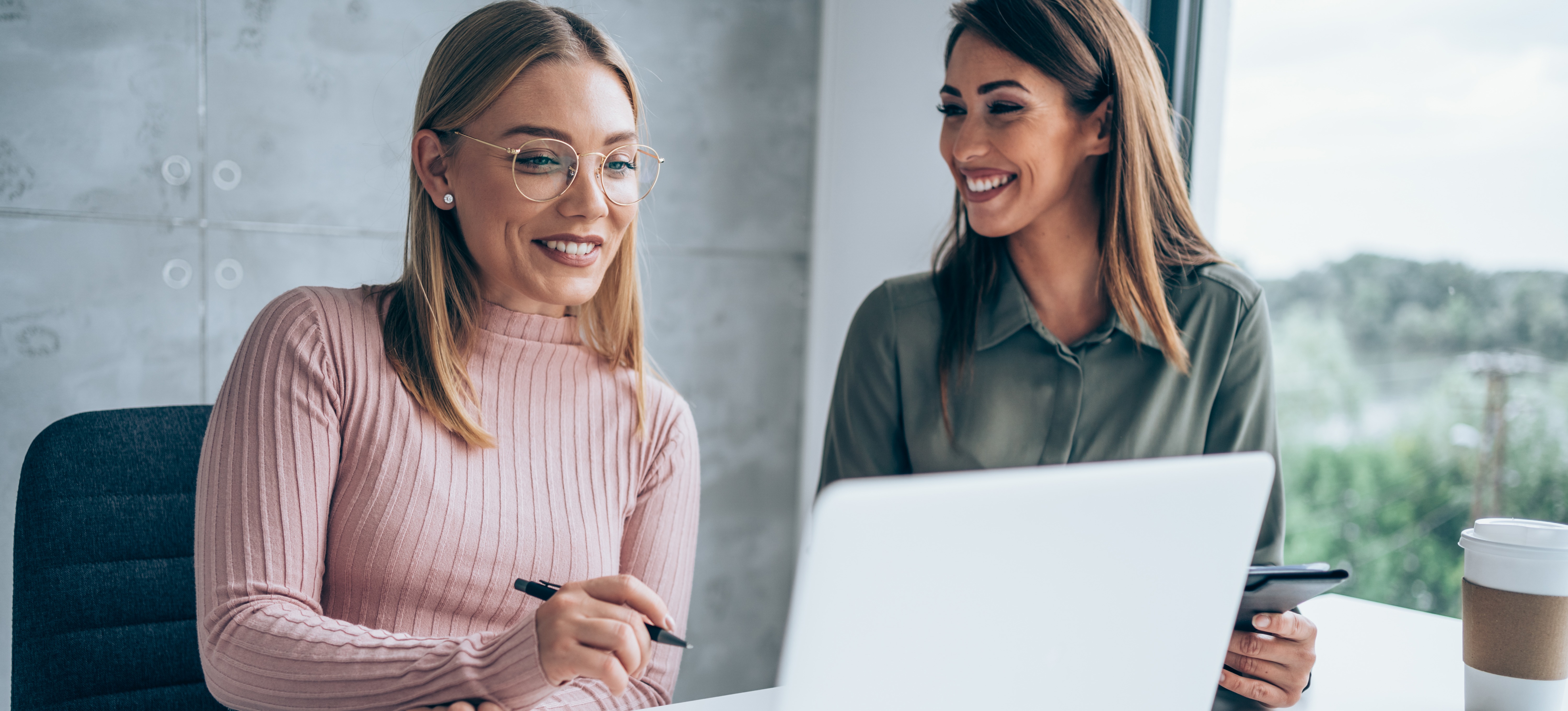 [Featured Image] Two social media marketing specialists sit at a desk using a laptop to work on a social marketing campaign together. ﻿
