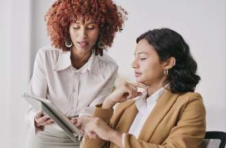 [Featured image] An employee approaches a member of middle management with a question about some information on her tablet.  
