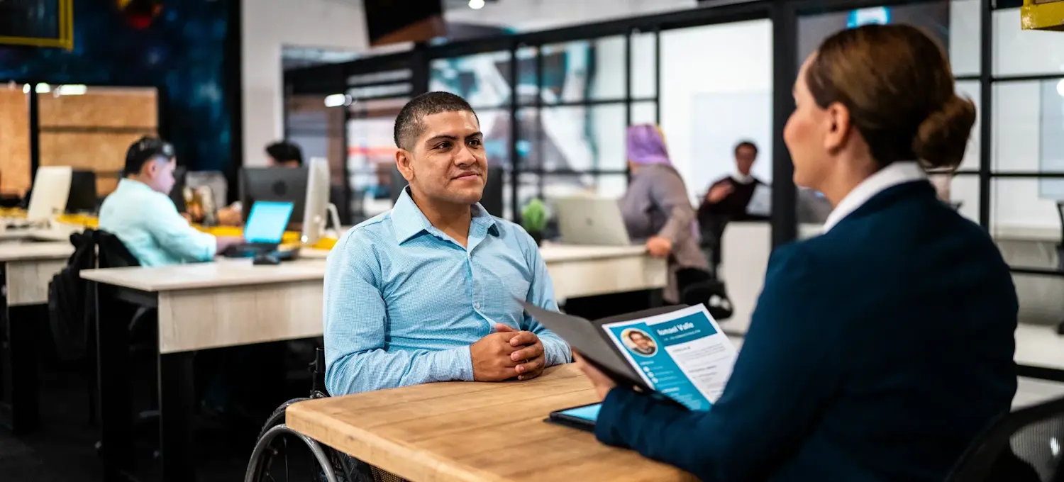 [Feature Image] A job candidate who uses a wheelchair responds to decision tree interview questions during a meeting with a recruiter in an open office space.