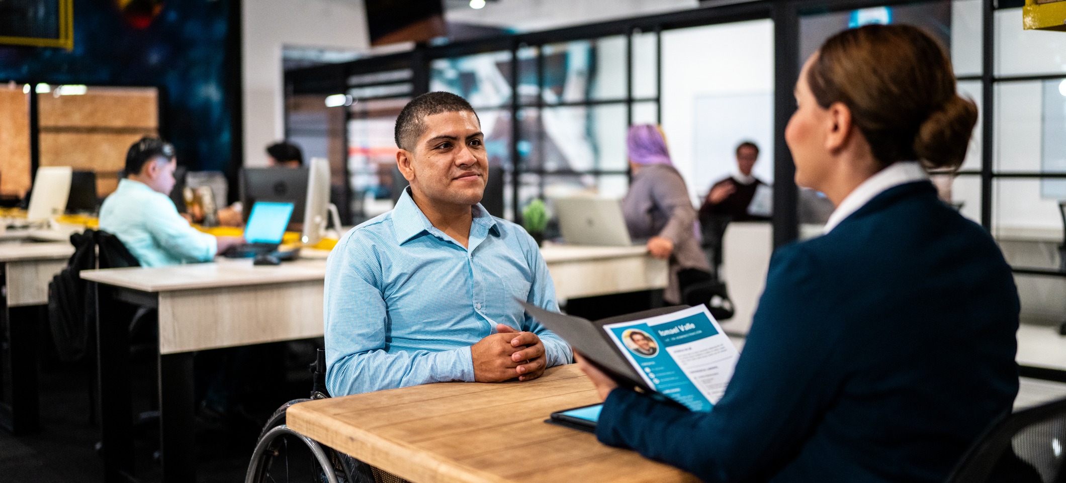 [Feature Image] A job candidate who uses a wheelchair responds to decision tree interview questions during a meeting with a recruiter in an open office space.