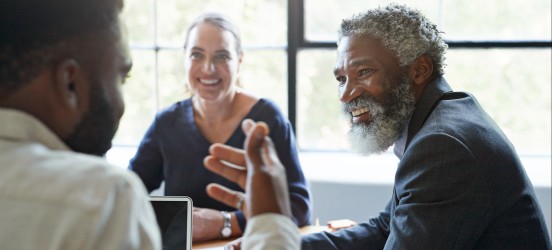 [Featured image]: People meet at a conference table with an office window in the background.