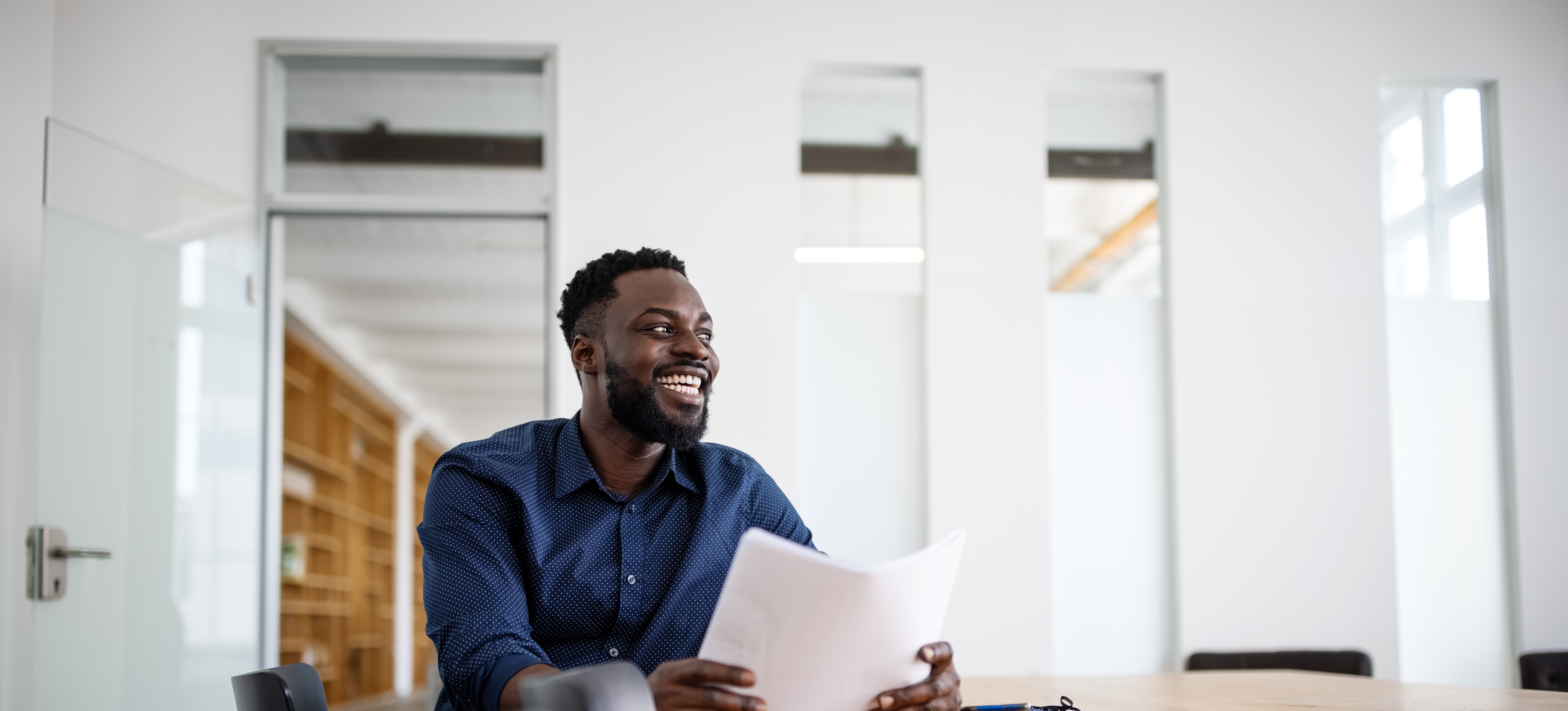 [Featured Image]  A person in a dark shirt sits at a long brown table reviewing their resume as they think about changing their career. 