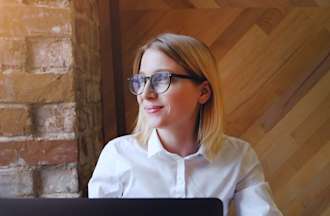 [Featured image] A female computer programmer, with blonde hair, wearing a white shirt and glasses.  She is sitting in front of her laptop. 