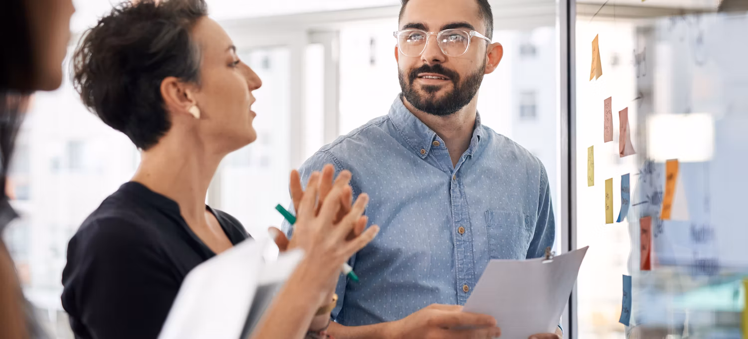 [Featured image] A marketing team discusses brand strategy in front of a whiteboard with sticky notes on it.