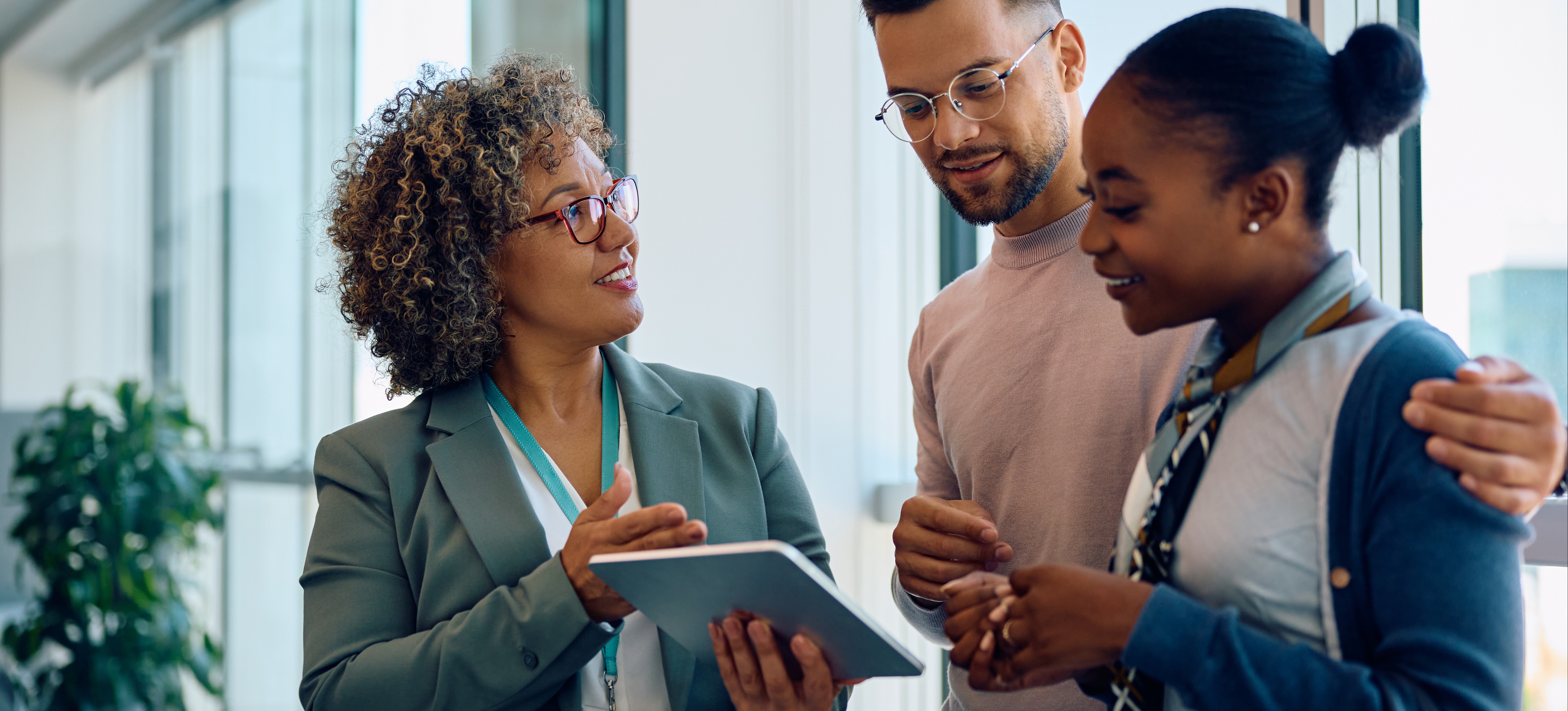 [Featured Image] A smiling professional shows a happy couple information on a tablet about their first home after figuring out the answer to the question, “Is real estate a good career.” 