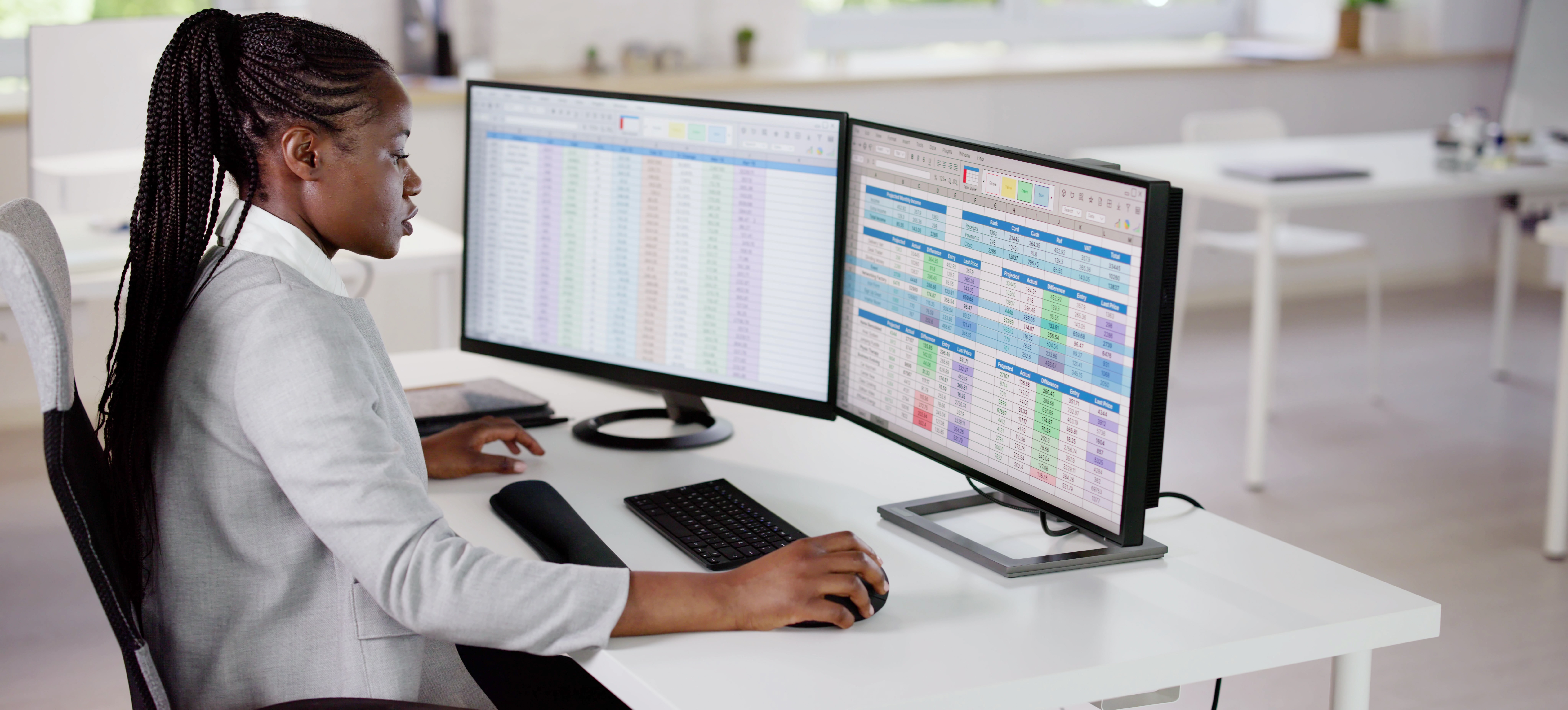 [Featured Image] A data analyst sits at their office desk analyzing spreadsheets on their two computer screens to gain data insights about their work.
