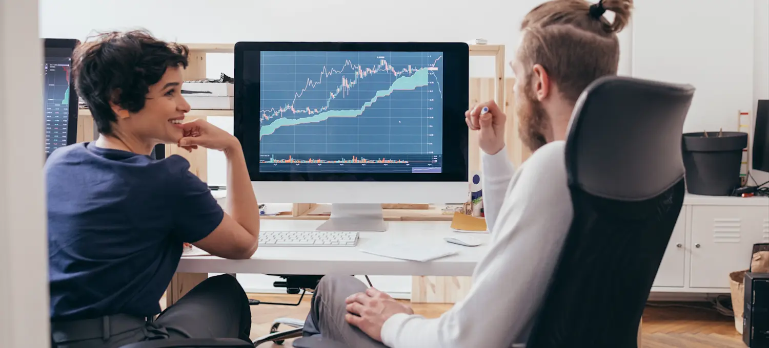 [Featured Image] A crypto mining engineer and a colleague discussing progress in an office environment, analyzing cryptocurrency mining charts on a computer.
