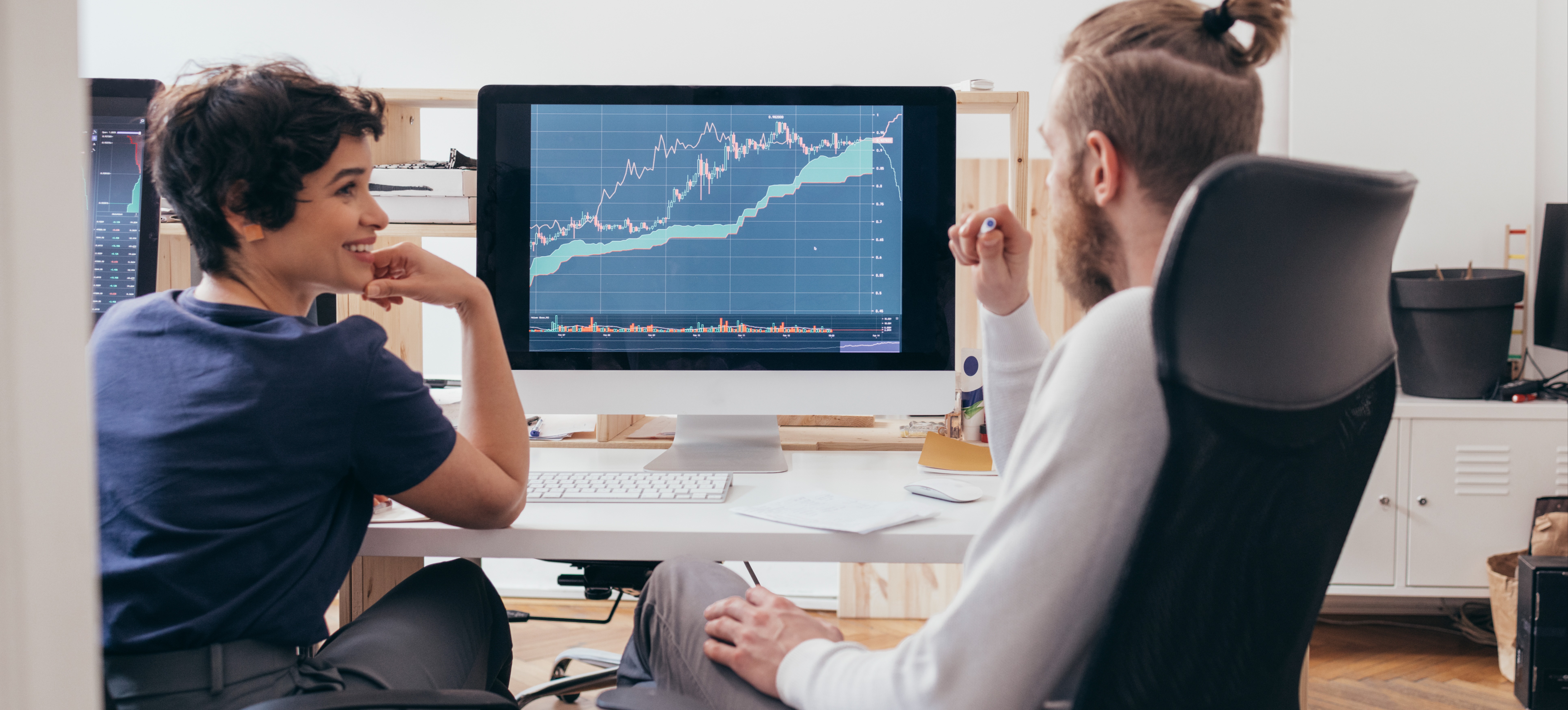 [Featured Image] A crypto mining engineer and a colleague discussing progress in an office environment, analyzing cryptocurrency mining charts on a computer.
