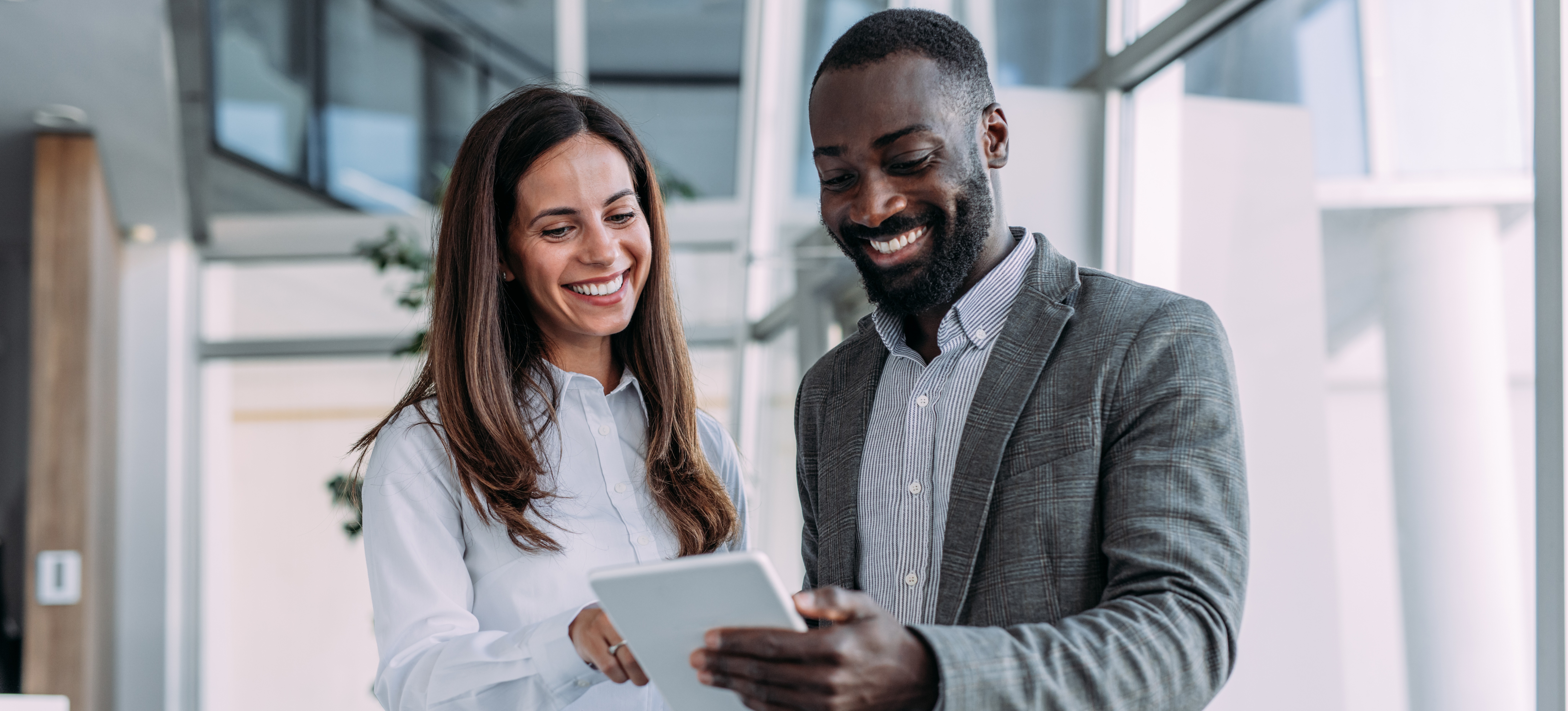 [Image en vedette] Deux collègues sourient en regardant une tablette et communiquent efficacement, ce qui est l'une des compétences clés recherchées.